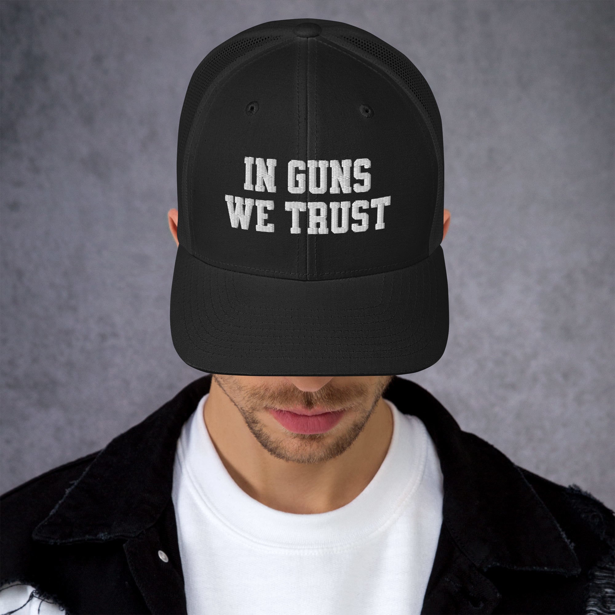 Person wearing a black cap with 'IN GUNS WE TRUST' text on a gray background