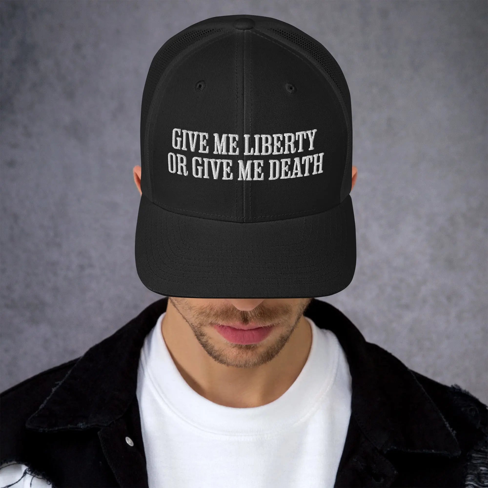 A man wearing a black patriotic trucker hat with the text "Give Me Liberty Or Give Me Death."