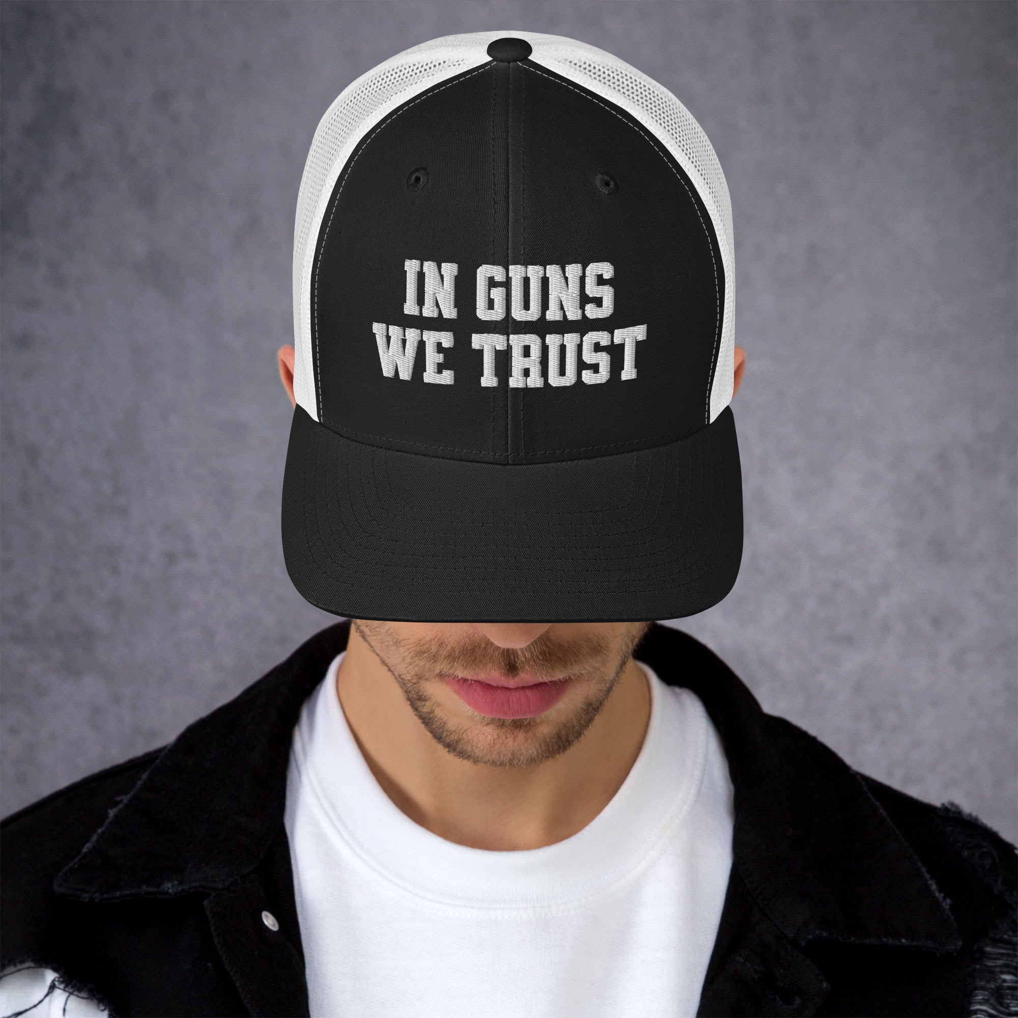 Person wearing a black and white cap with 'IN GUNS WE TRUST' text on a gray background