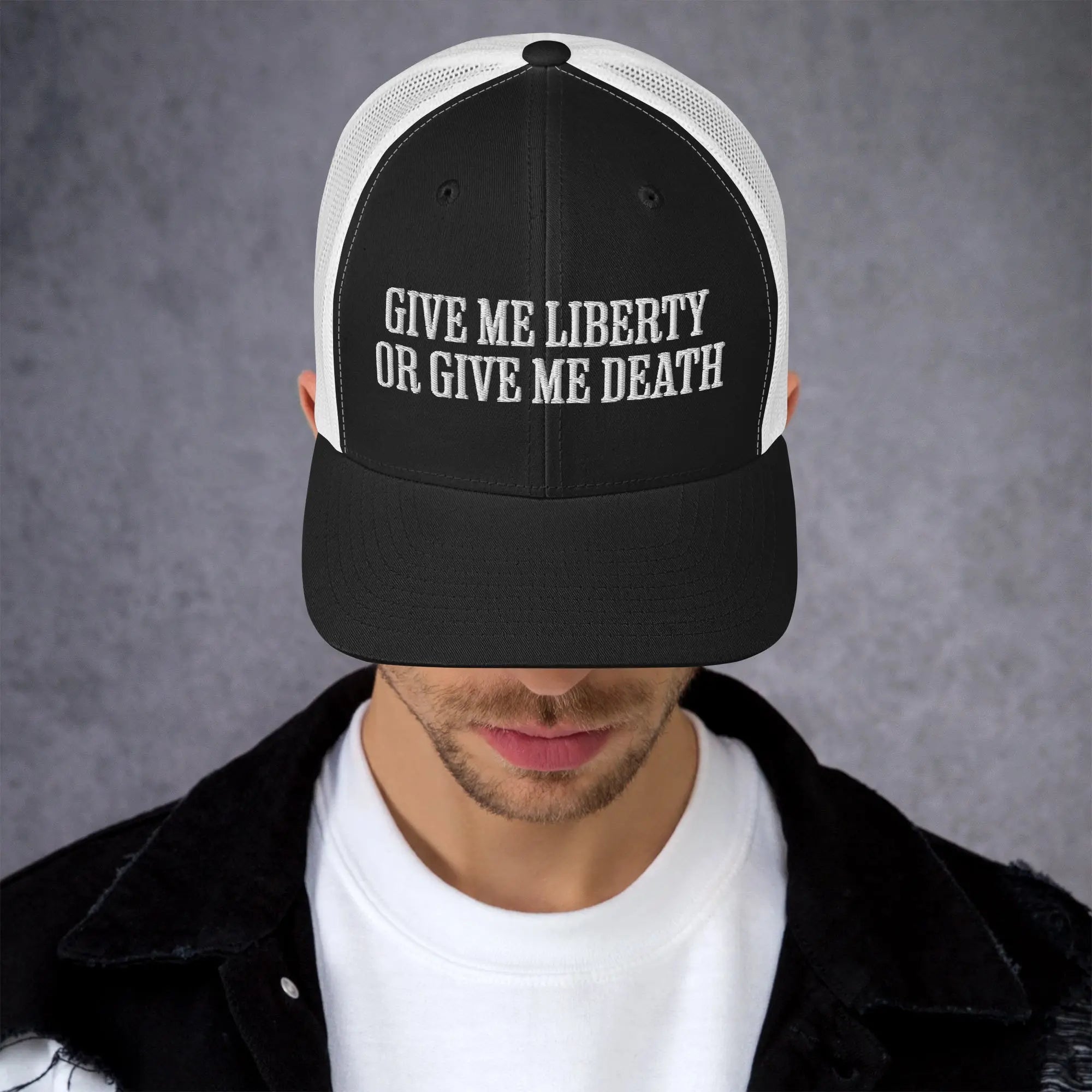 A man wearing a black and white patriotic trucker hat with the text "Give Me Liberty Or Give Me Death."