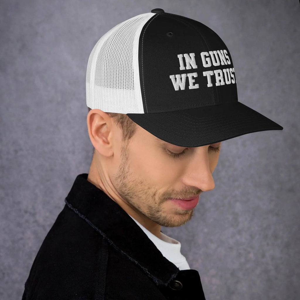 Man wearing a black and white cap with 'IN GUNS WE TRUST' text on a gray background