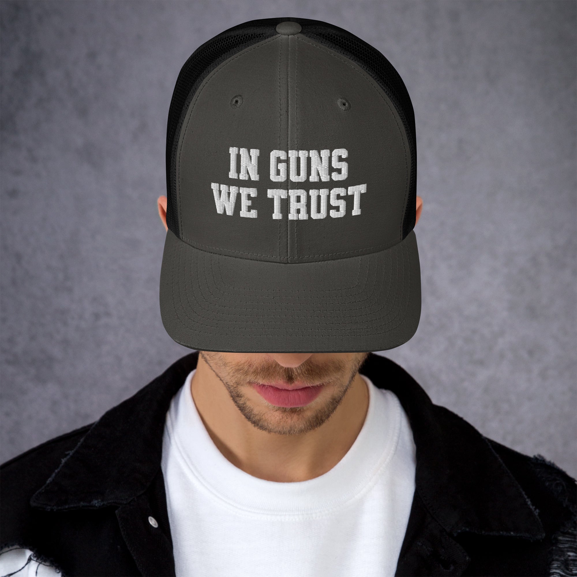 Person wearing a black cap with 'IN GUNS WE TRUST' text on a gray background