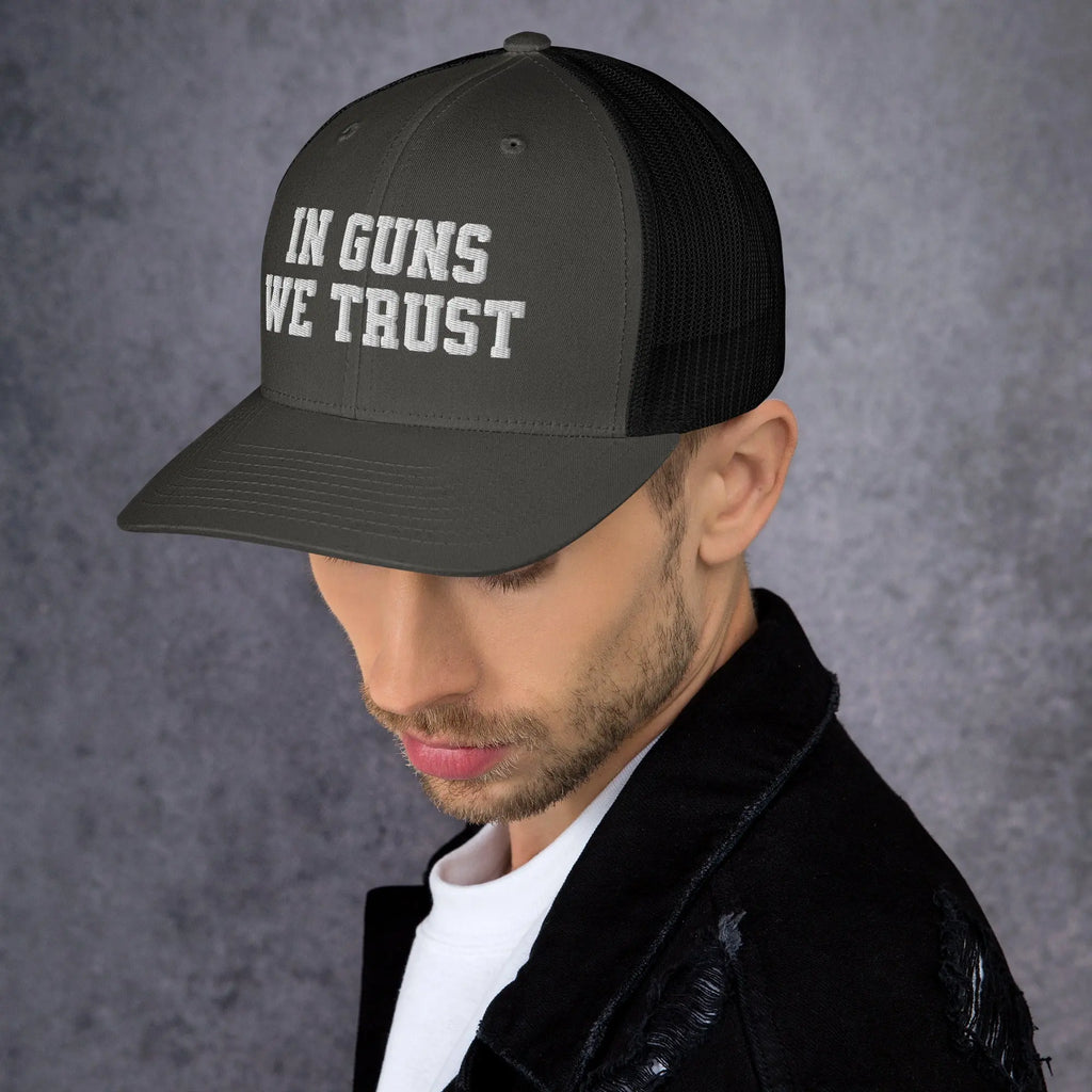 Man wearing a cap with 'IN GUNS WE TRUST' text on a gray background