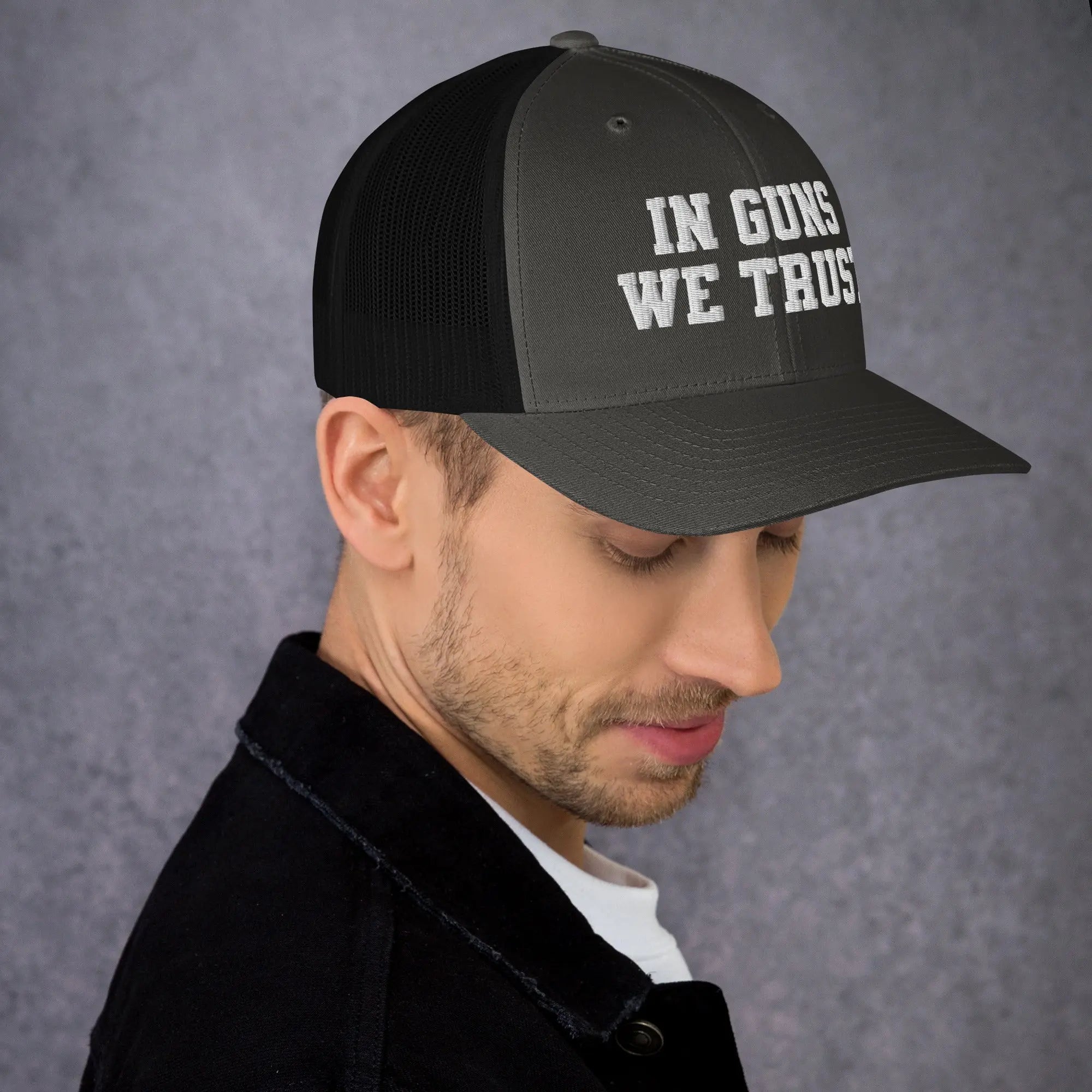 Man wearing a black cap with 'IN GUNS WE TRUST' text on a gray background