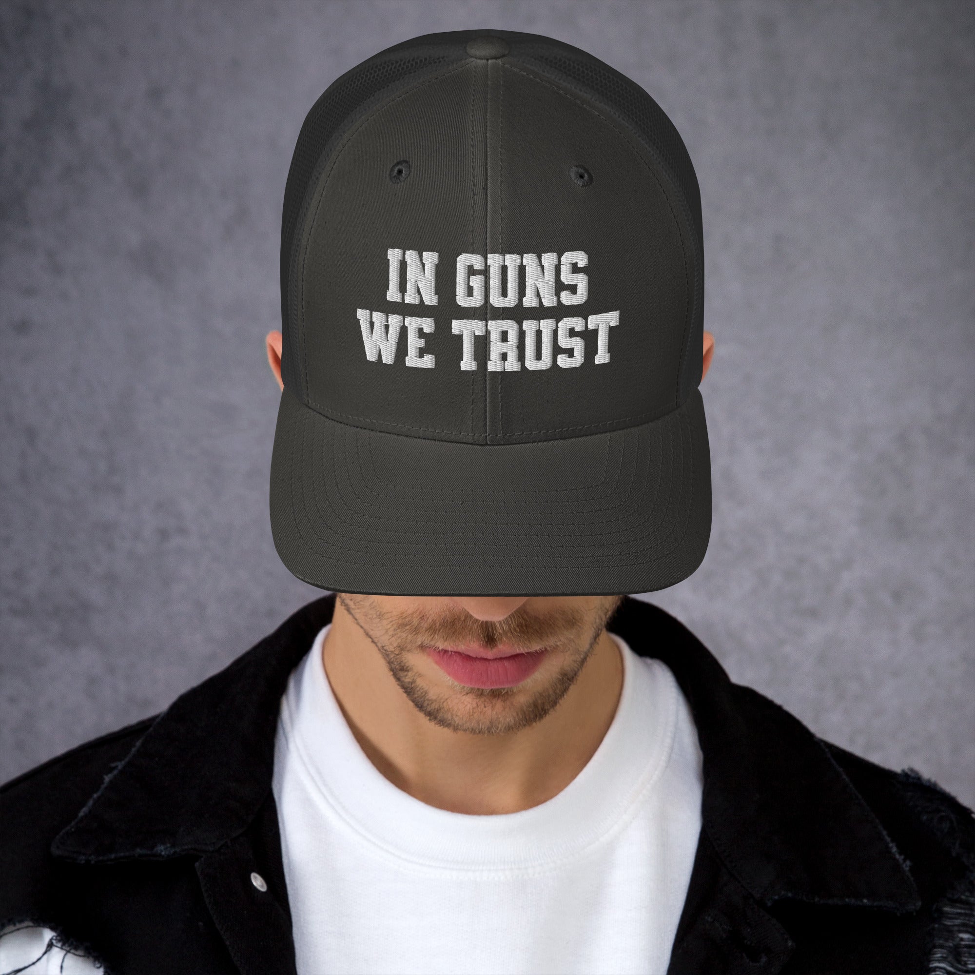 Person wearing a black cap with 'IN GUNS WE TRUST' text on a gray background