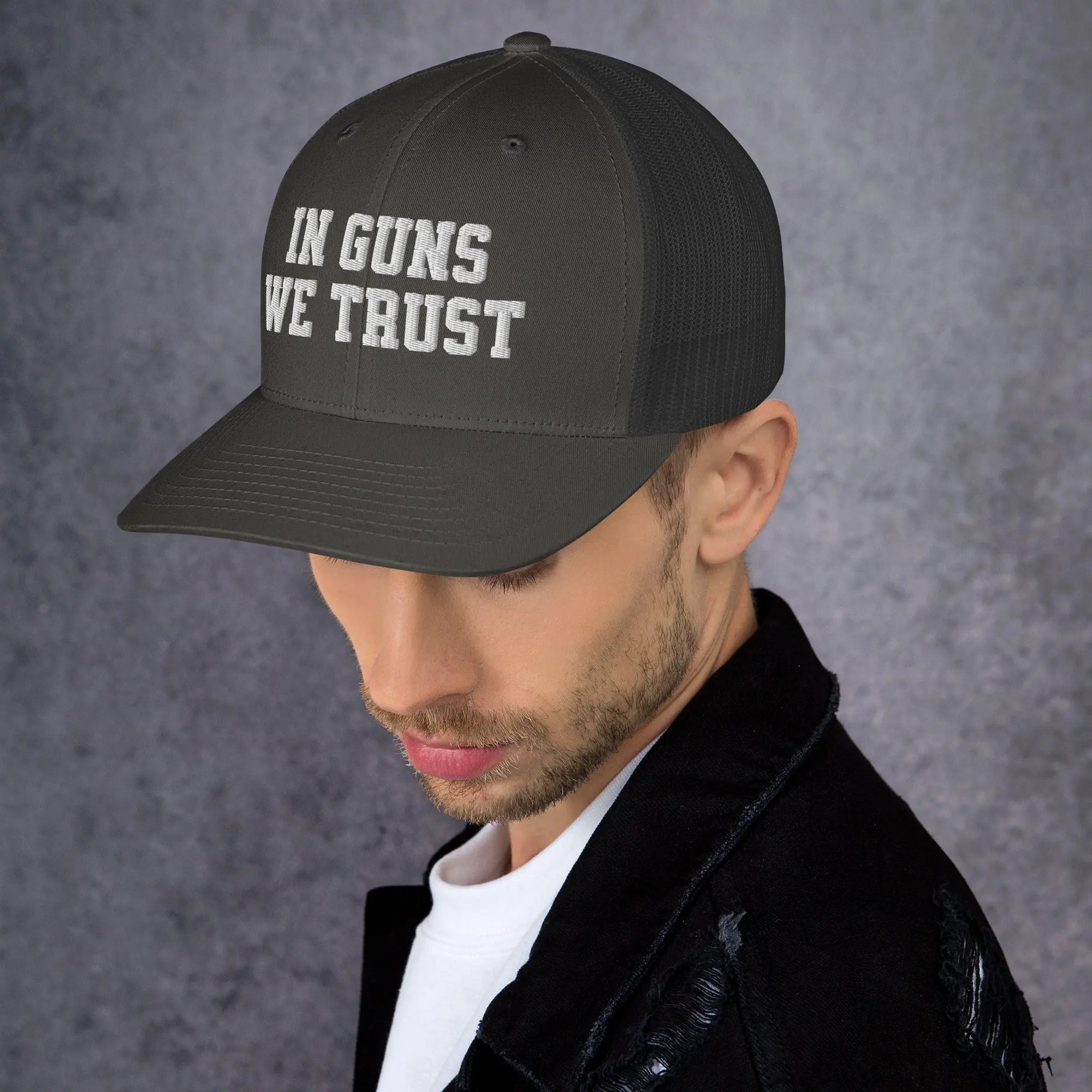 Man wearing a black cap with 'IN GUNS WE TRUST' text on a gray background
