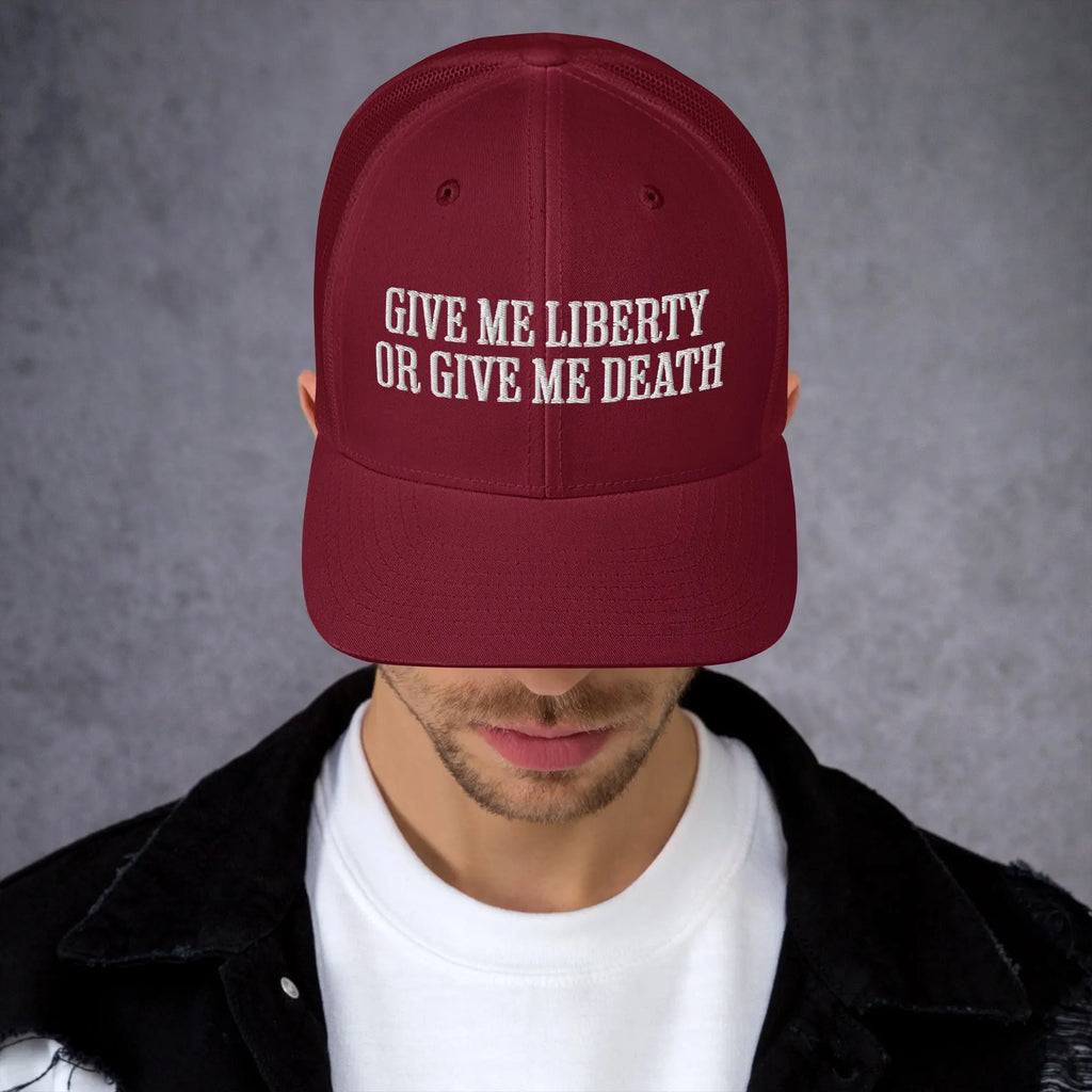 A man wearing a cranberry-colored patriotic trucker hat with the text "Give Me Liberty Or Give Me Death."