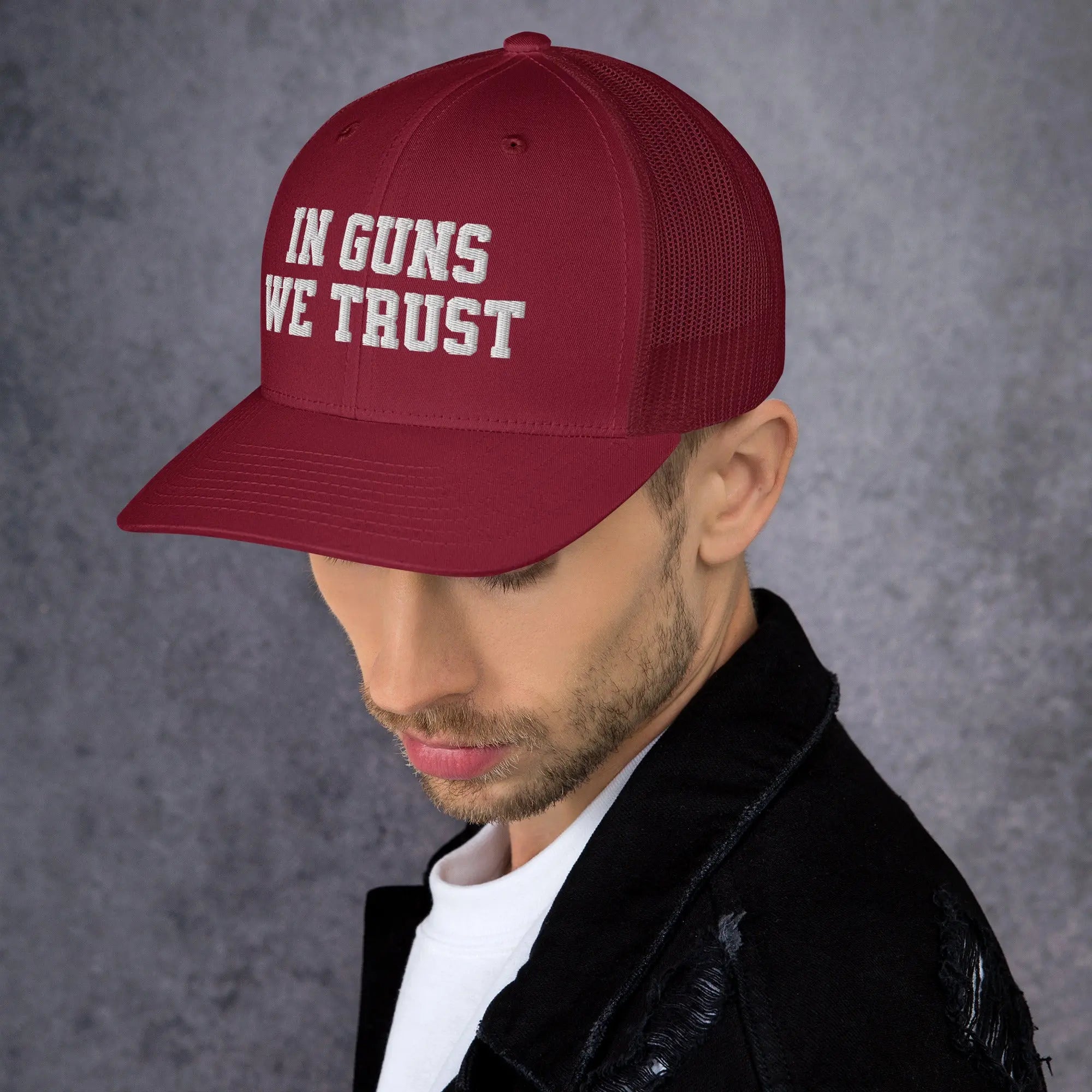 Man wearing a red cap with 'IN GUNS WE TRUST' text on a gray background