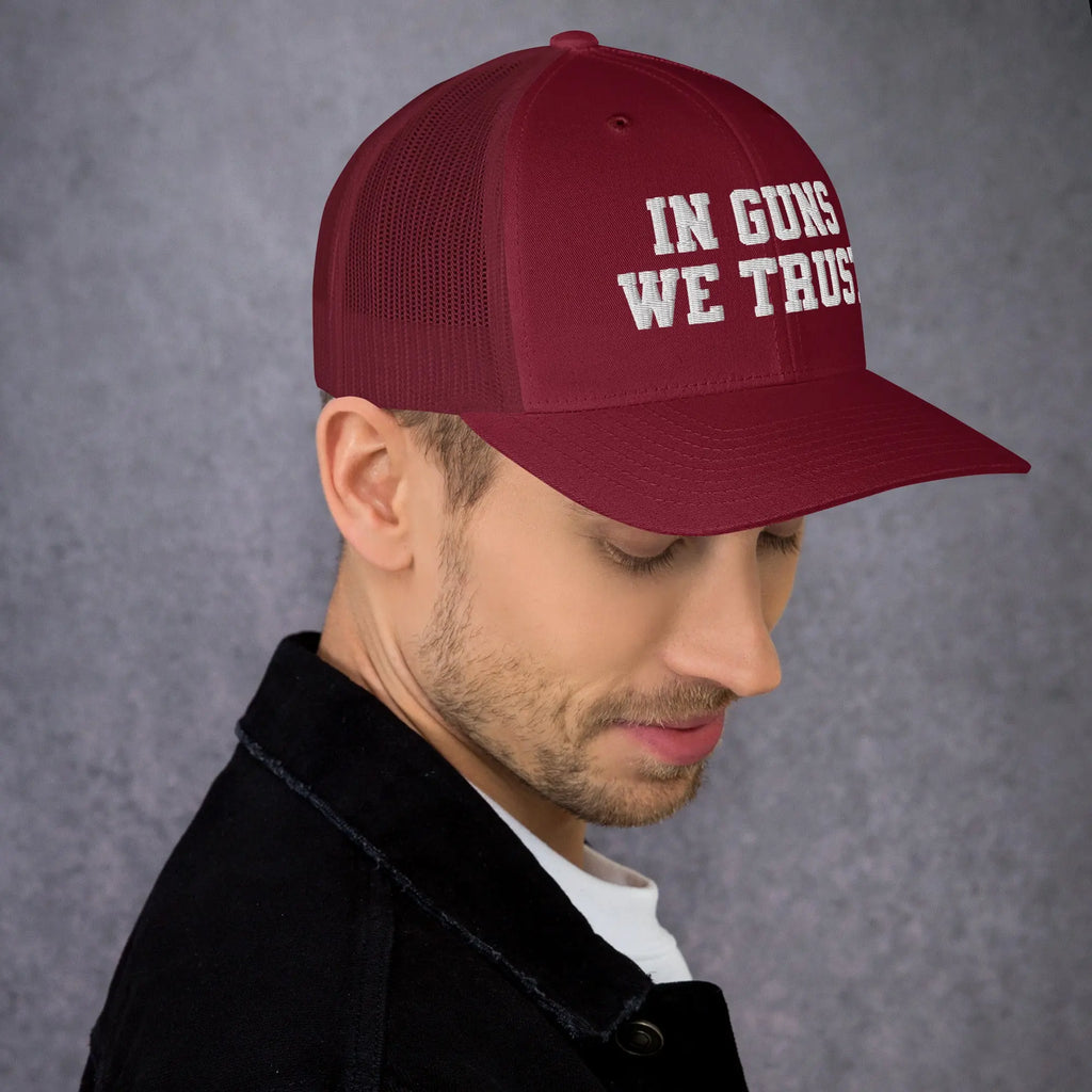 Man wearing a red cap with 'IN GUNS WE TRUST' text on a gray background