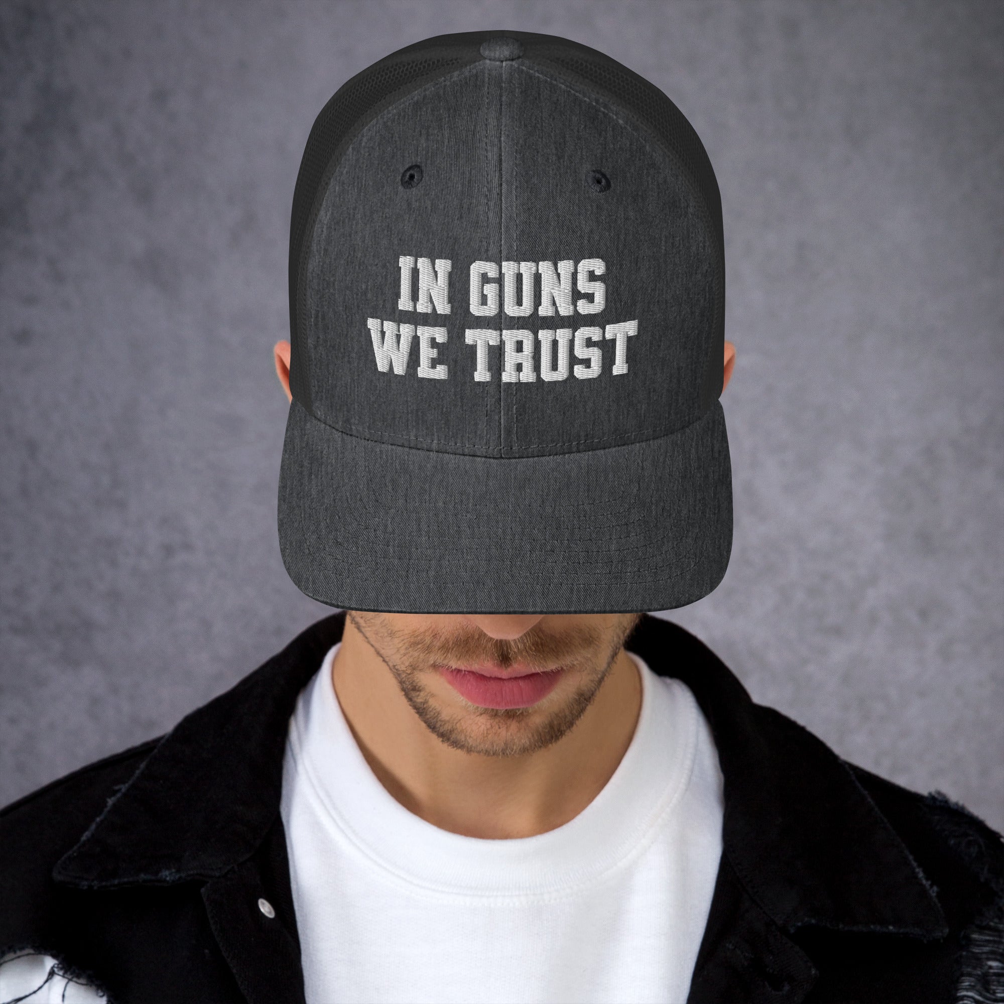 Person wearing a cap with 'IN GUNS WE TRUST' text on a gray background