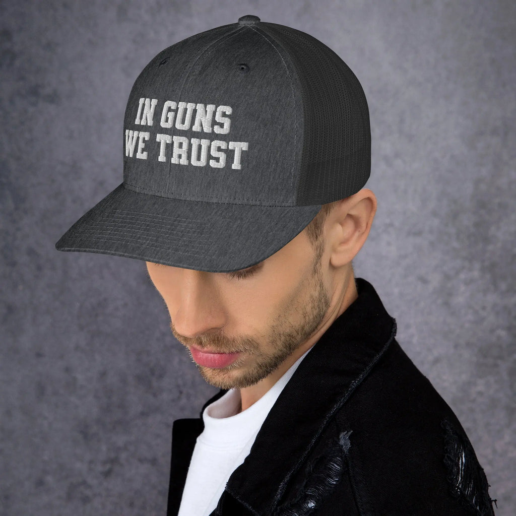 Man wearing a black cap with 'IN GUNS WE TRUST' text on a gray background