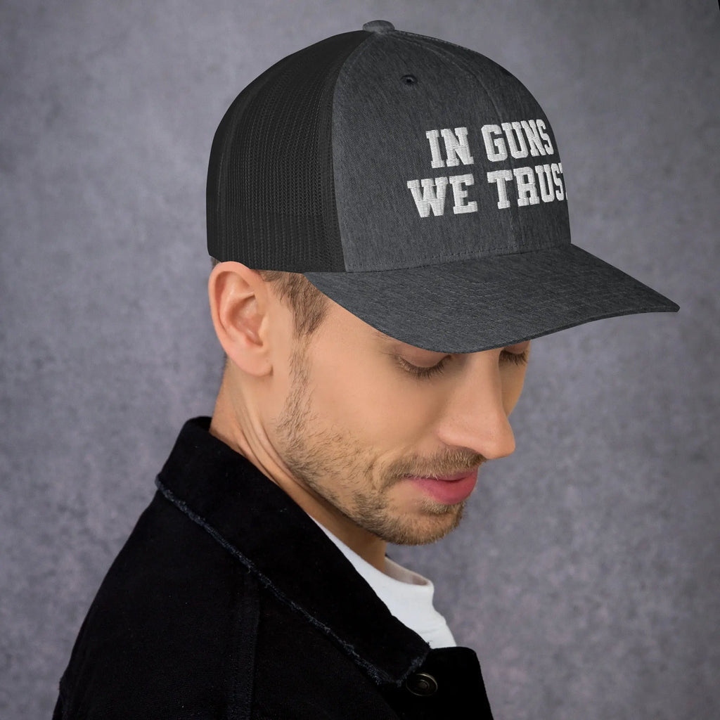 Man wearing a black cap with 'IN GUNS WE TRUST' text on a gray background