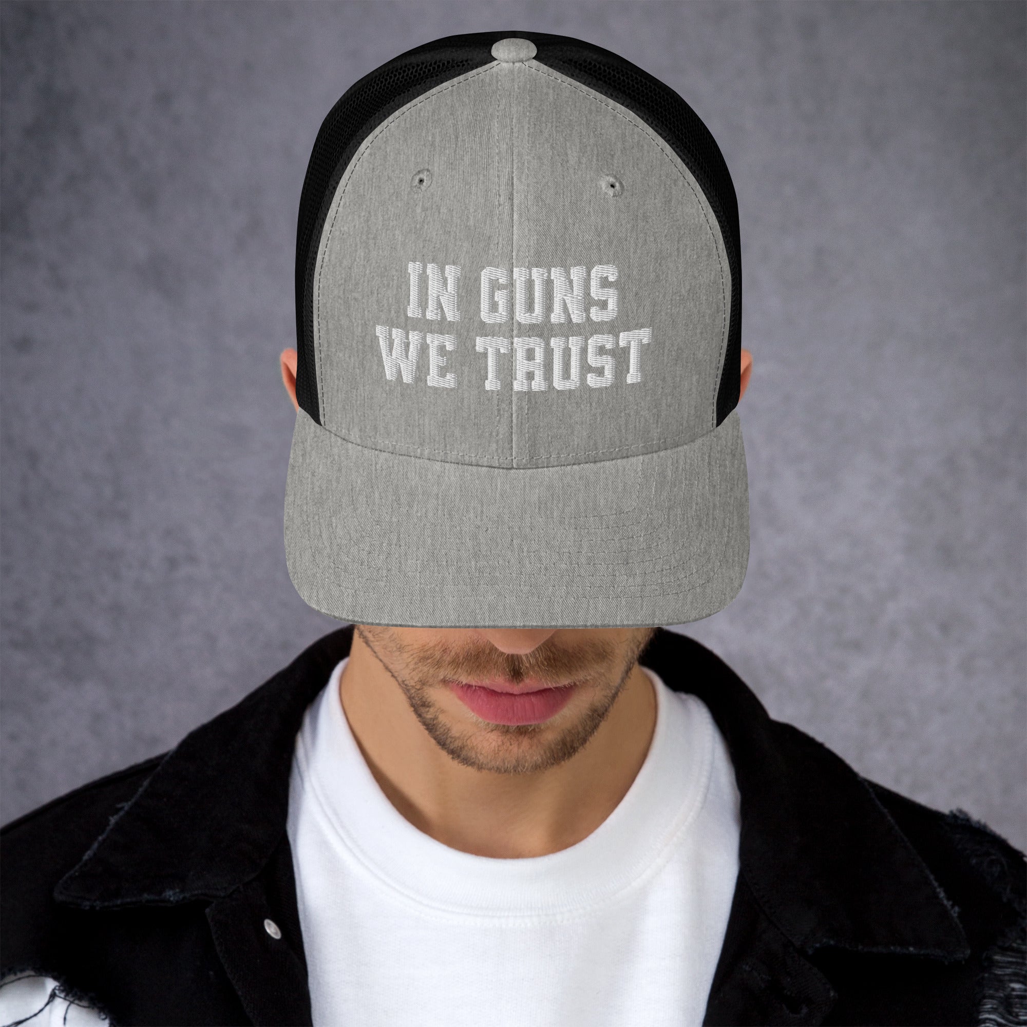 Person wearing a cap with 'IN GUNS WE TRUST' text on a gray background