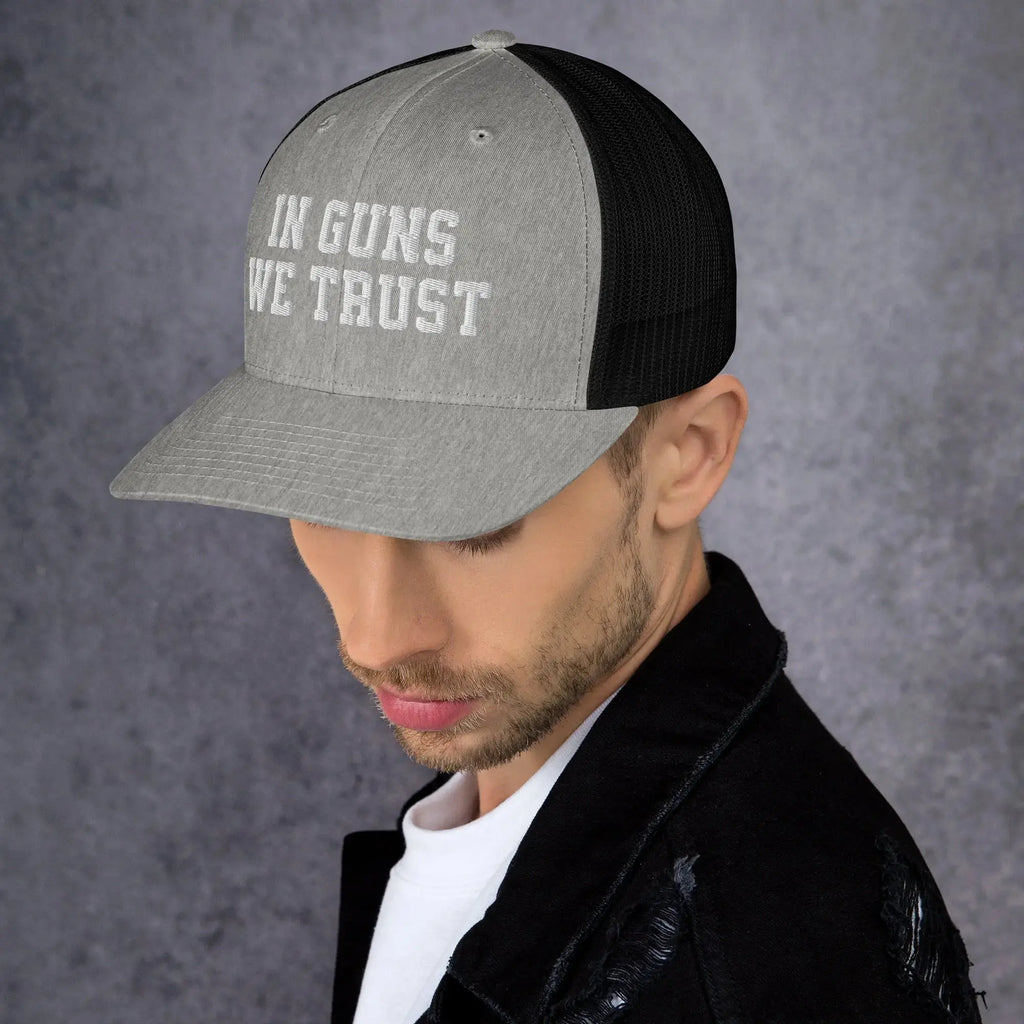 Man wearing a cap with 'IN GUNS WE TRUST' text on a gray background