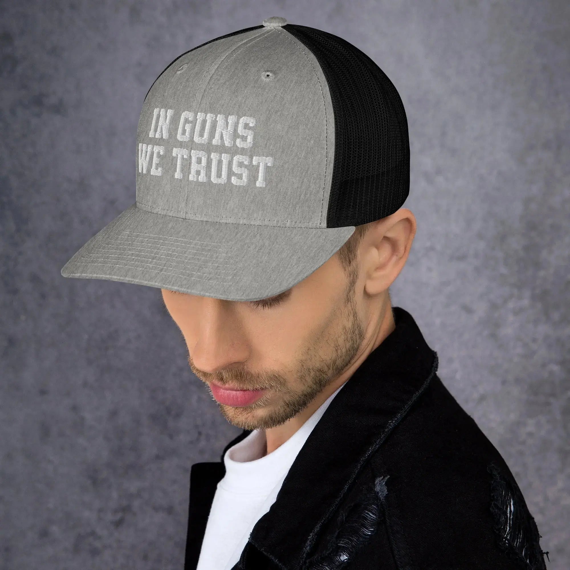 Man wearing a cap with 'IN GUNS WE TRUST' text on a gray background