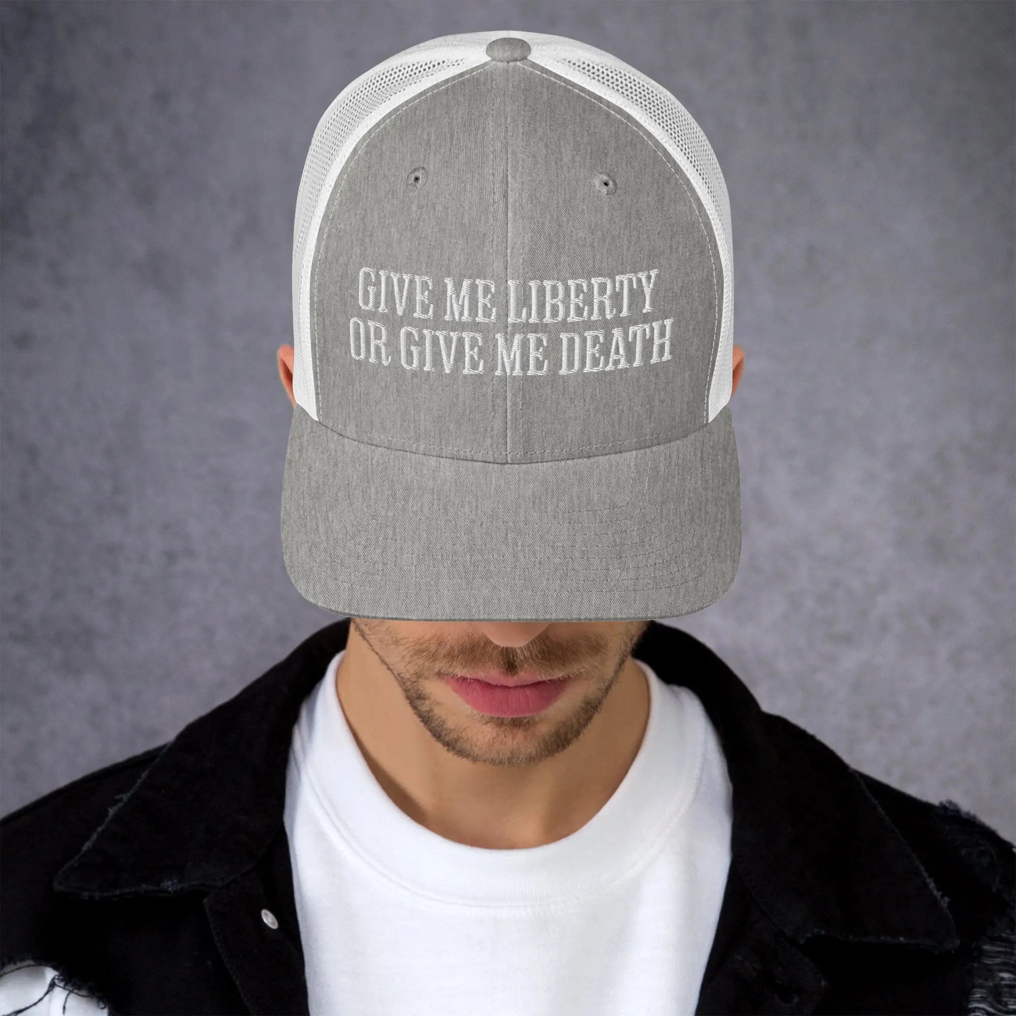 A man wearing a heather grey amd white patriotic trucker hat with the text "Give Me Liberty Or Give Me Death."