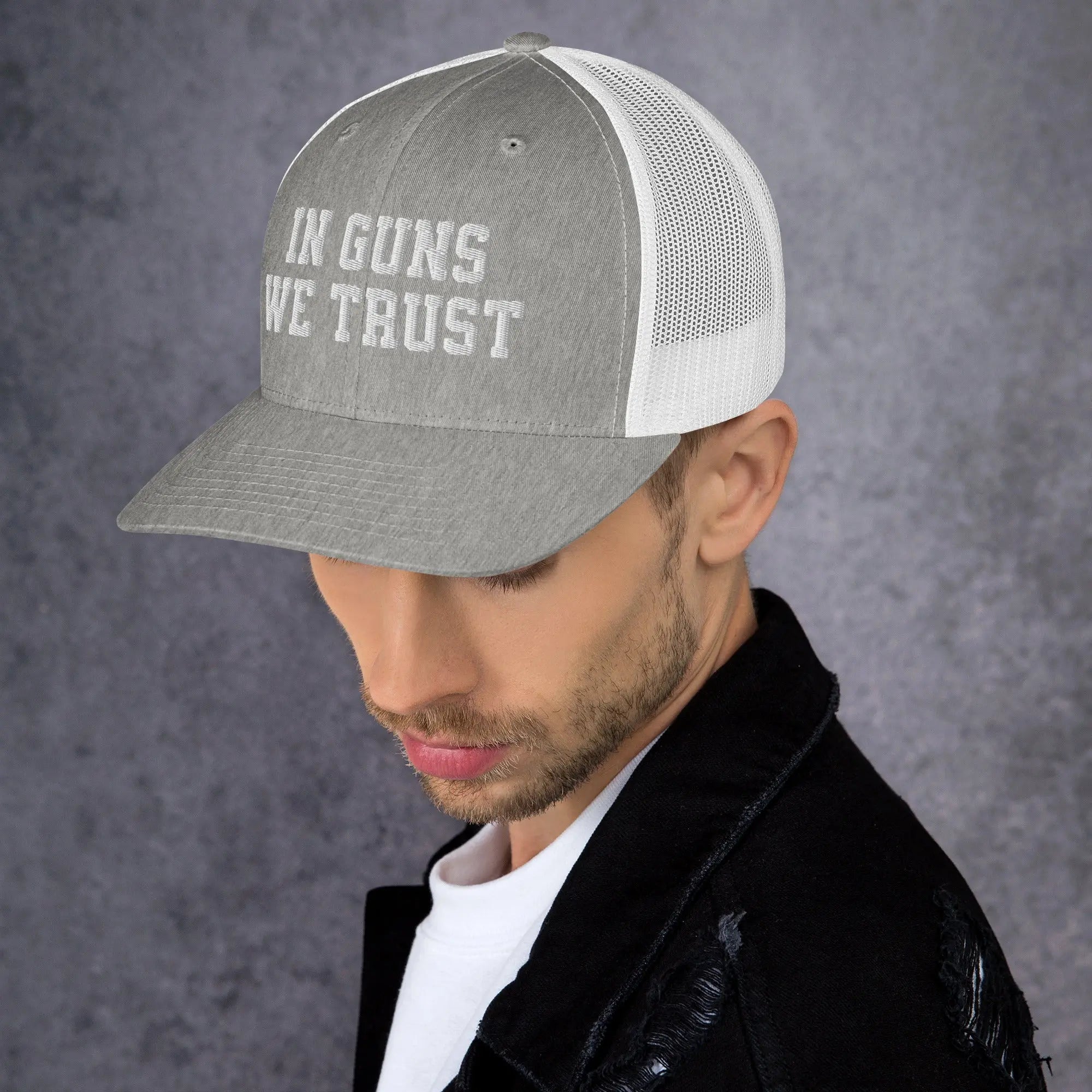 Man wearing a cap with 'IN GUNS WE TRUST' text against a gray background