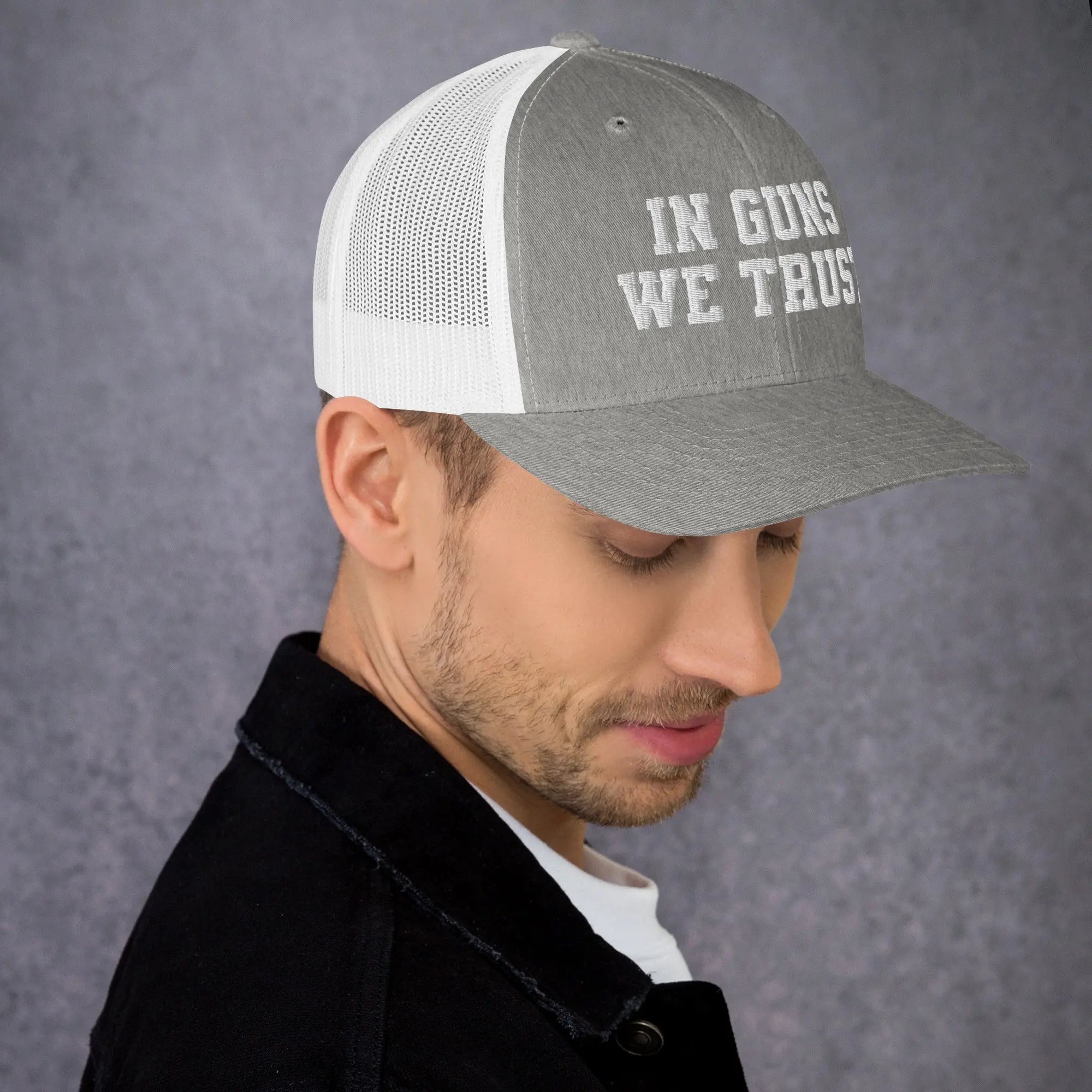 Man wearing a gray and white cap with 'IN GUNS WE TRUST' text on a gray background
