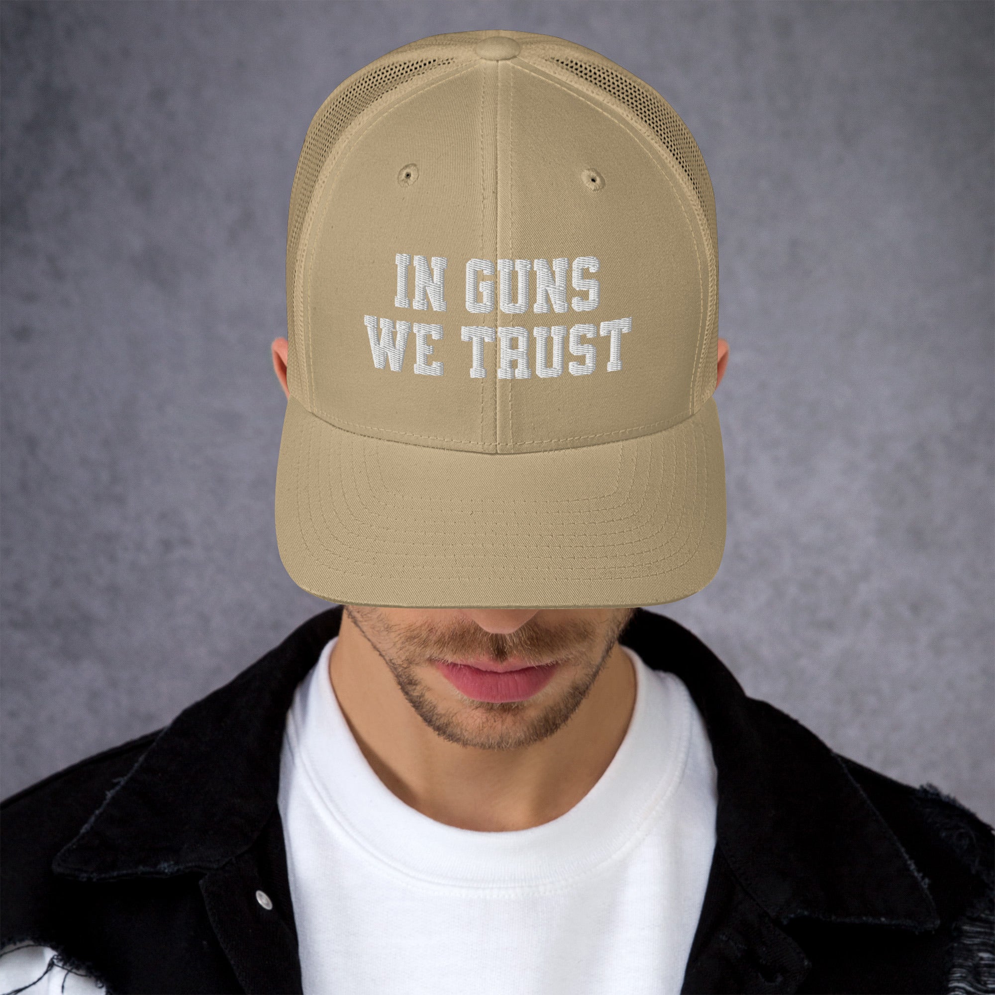 Person wearing a beige cap with 'IN GUNS WE TRUST' text on a gray background