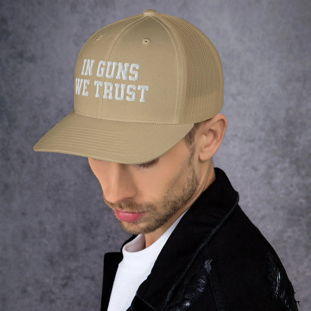 Man wearing a beige cap with 'IN GUNS WE TRUST' text on a gray background