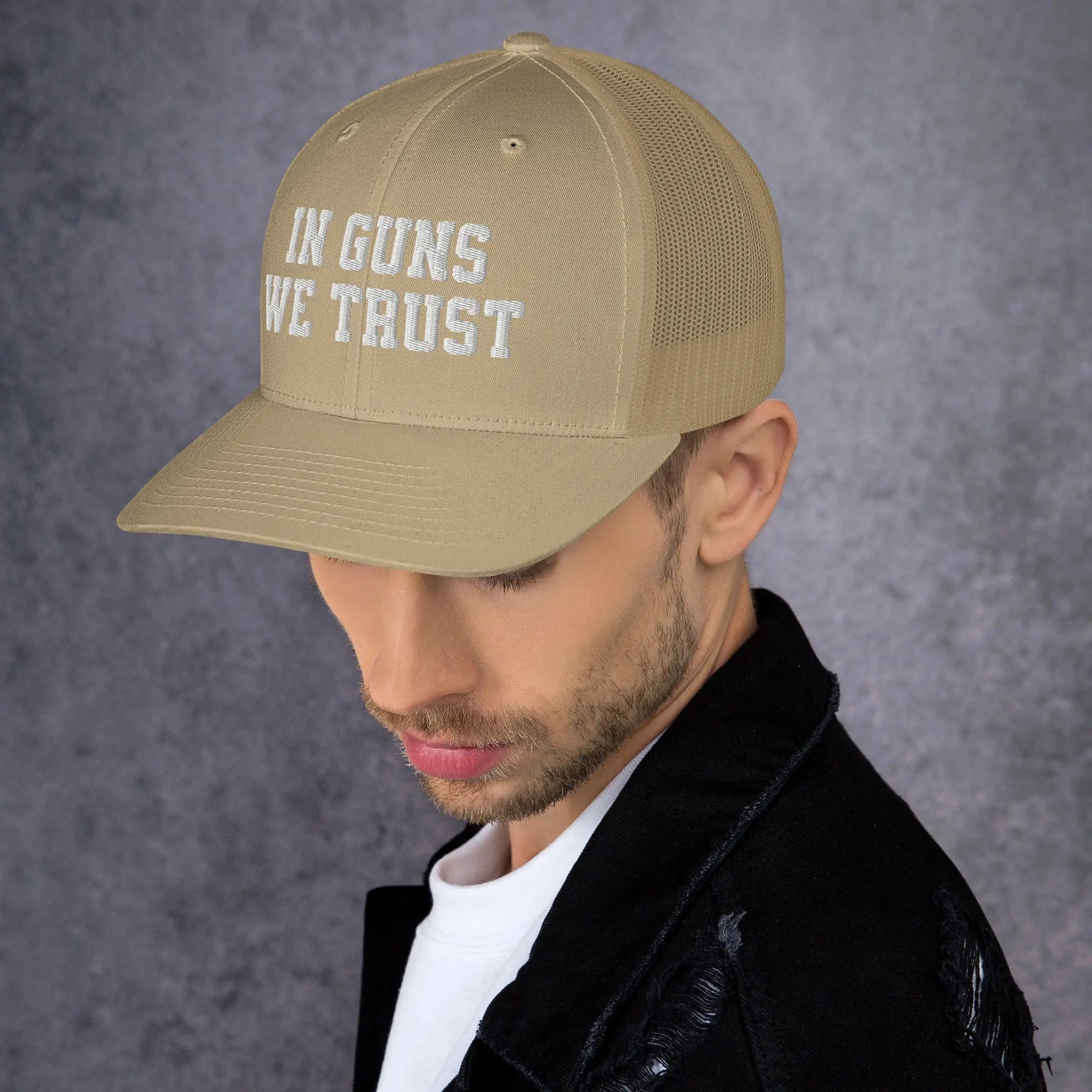 Man wearing a beige cap with 'IN GUNS WE TRUST' text on a gray background