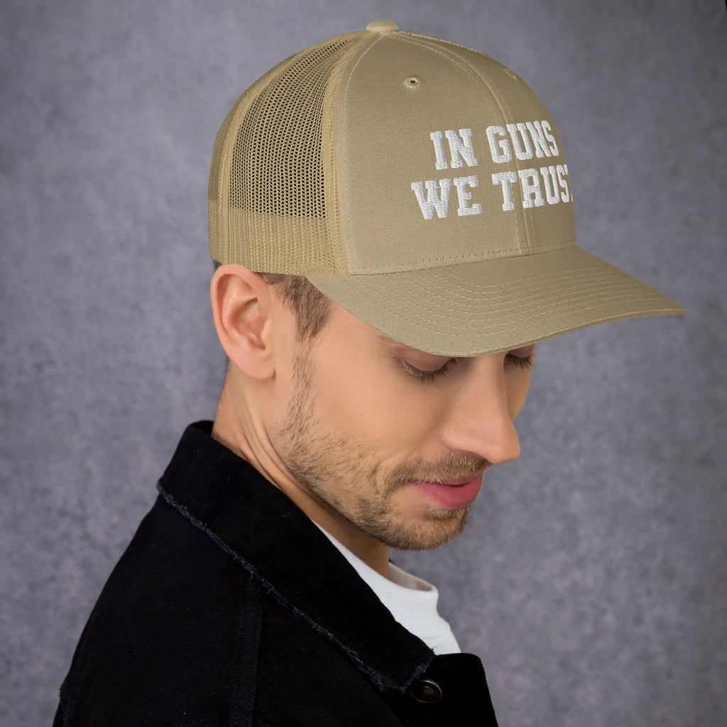 Man wearing a tan cap with 'IN GUNS WE TRUST' text on a gray background