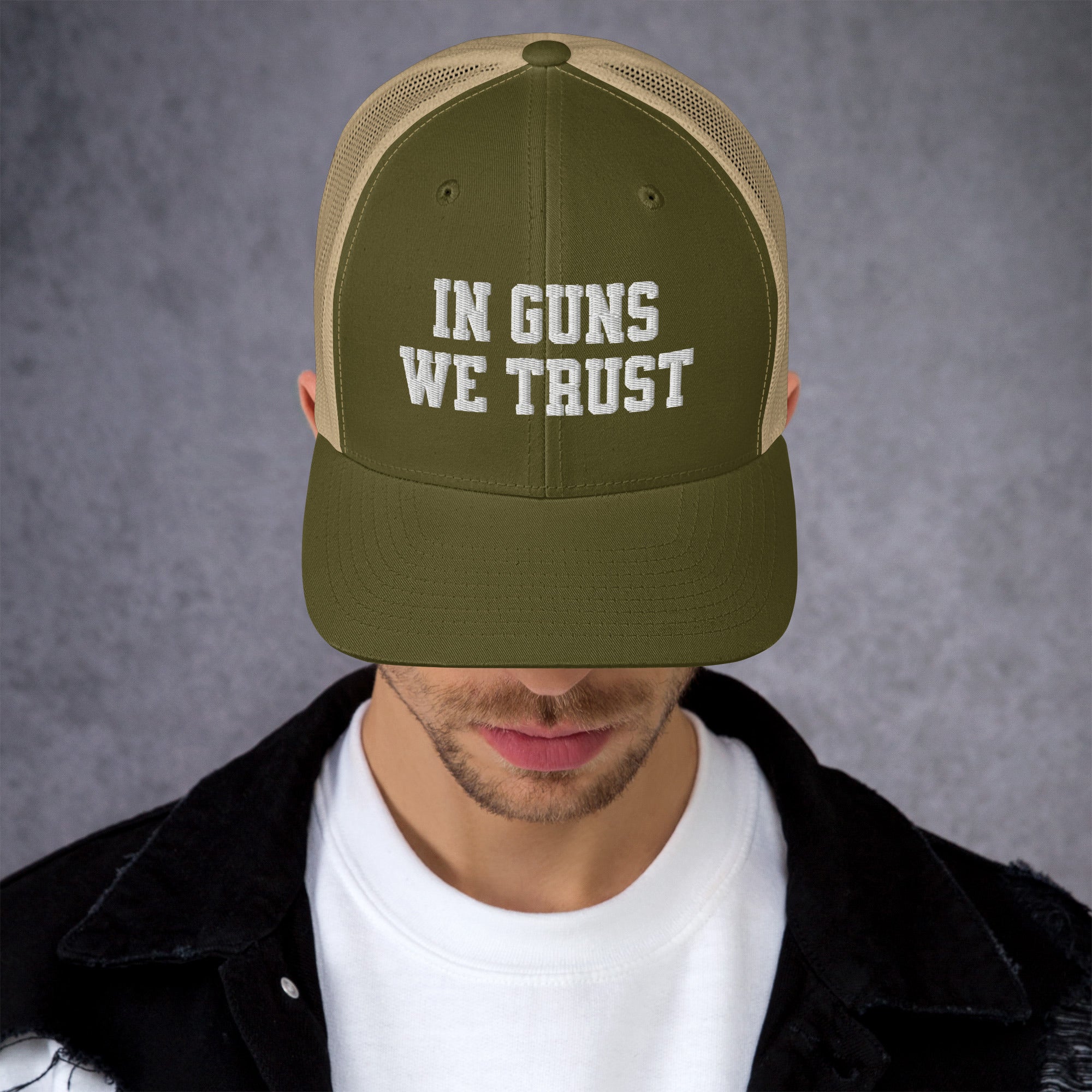 Person wearing a green and beige cap with 'IN GUNS WE TRUST' text on a gray background
