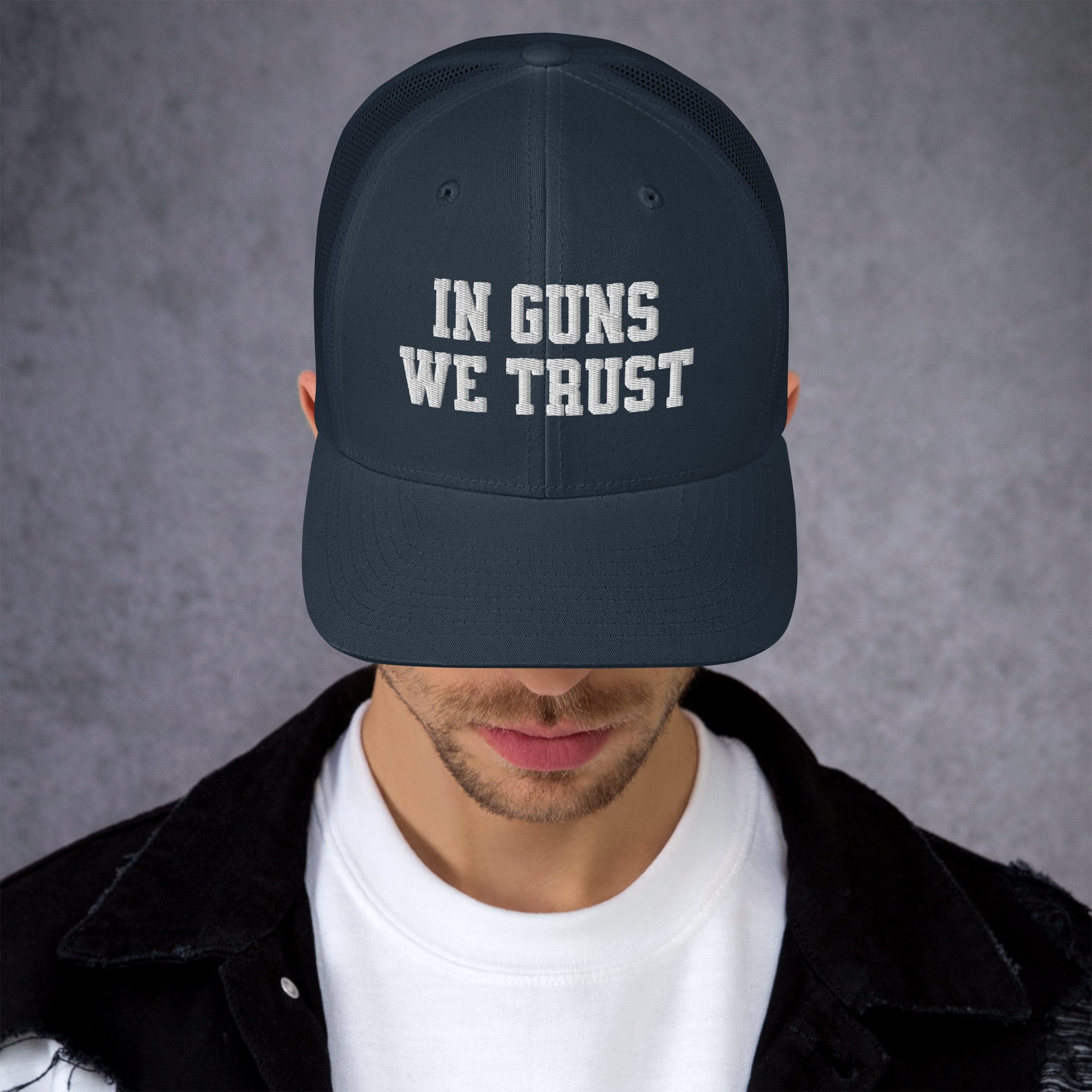 Person wearing a black cap with 'IN GUNS WE TRUST' text on a gray background
