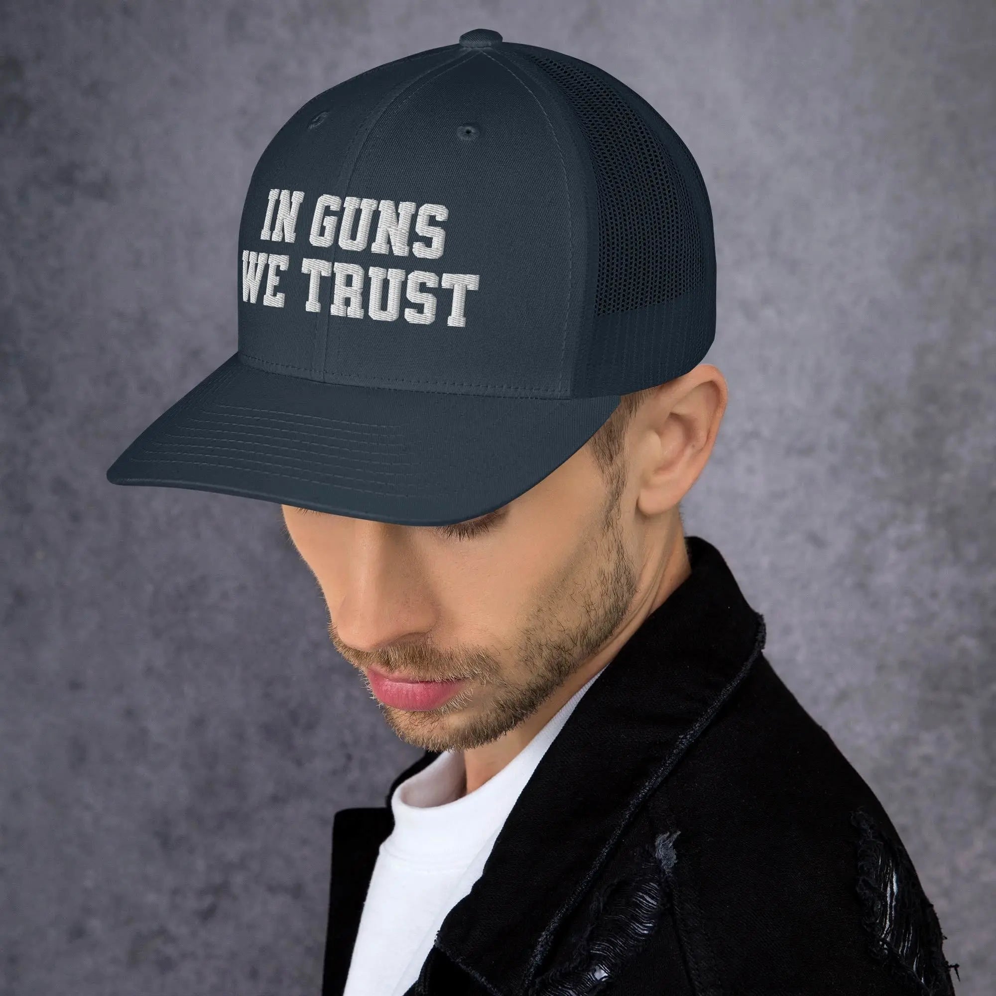 Man wearing a black cap with 'IN GUNS WE TRUST' text on a gray background
