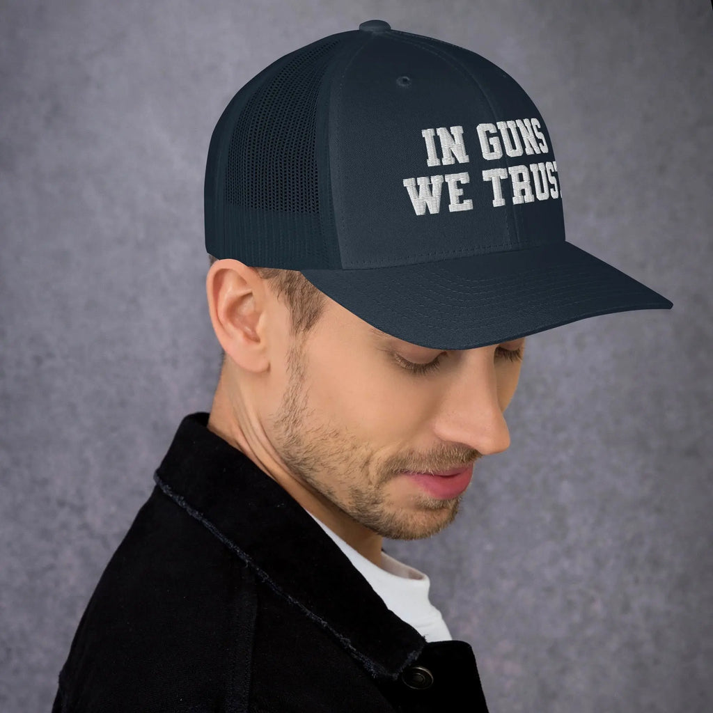 Man wearing a black cap with 'IN GUNS WE TRUST' text on a gray background