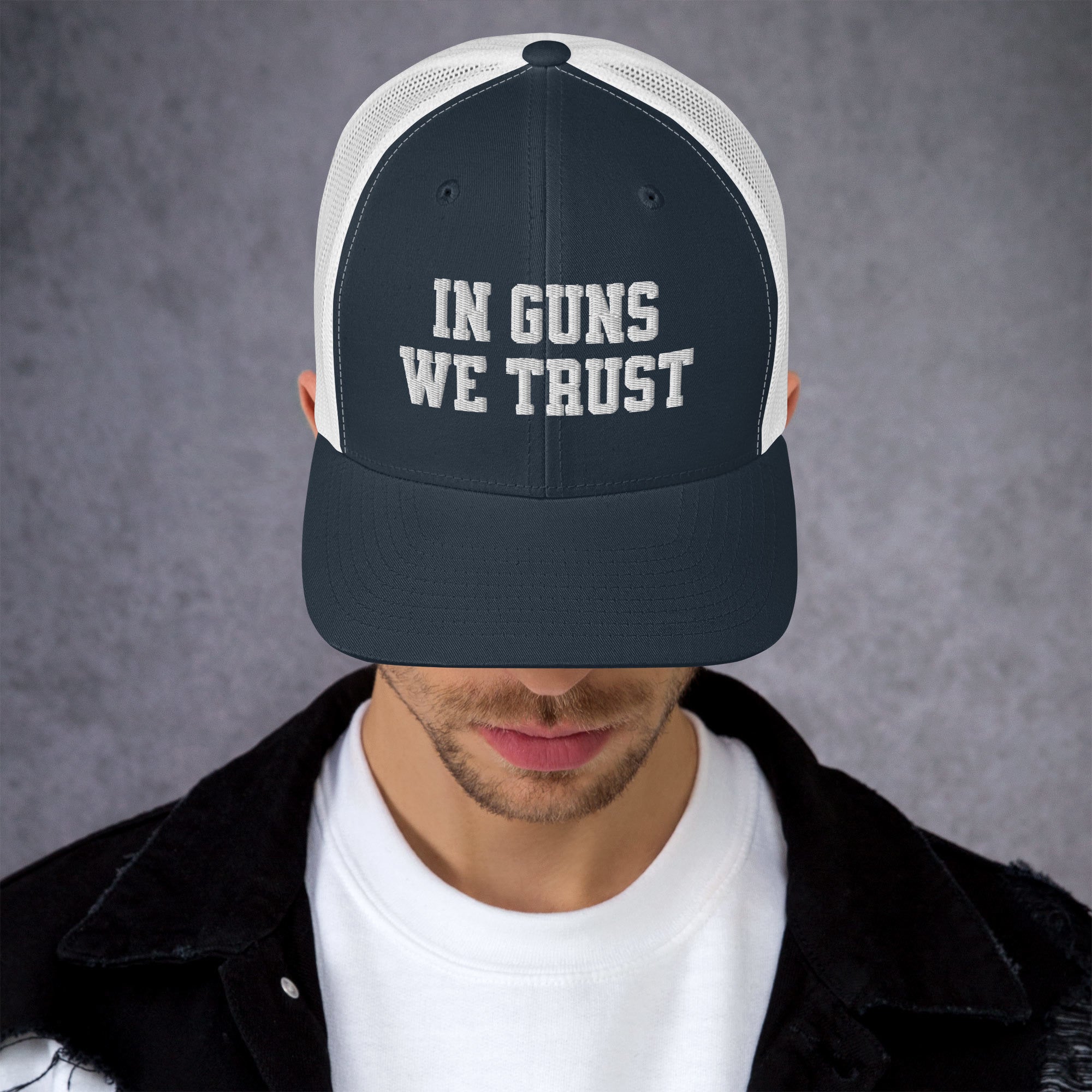 Person wearing a cap with 'IN GUNS WE TRUST' text on a gray background