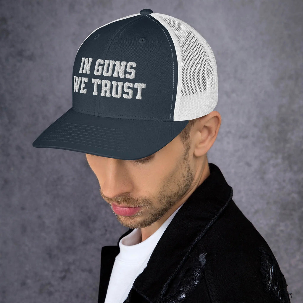 Man wearing a cap with 'IN GUNS WE TRUST' text on a gray background