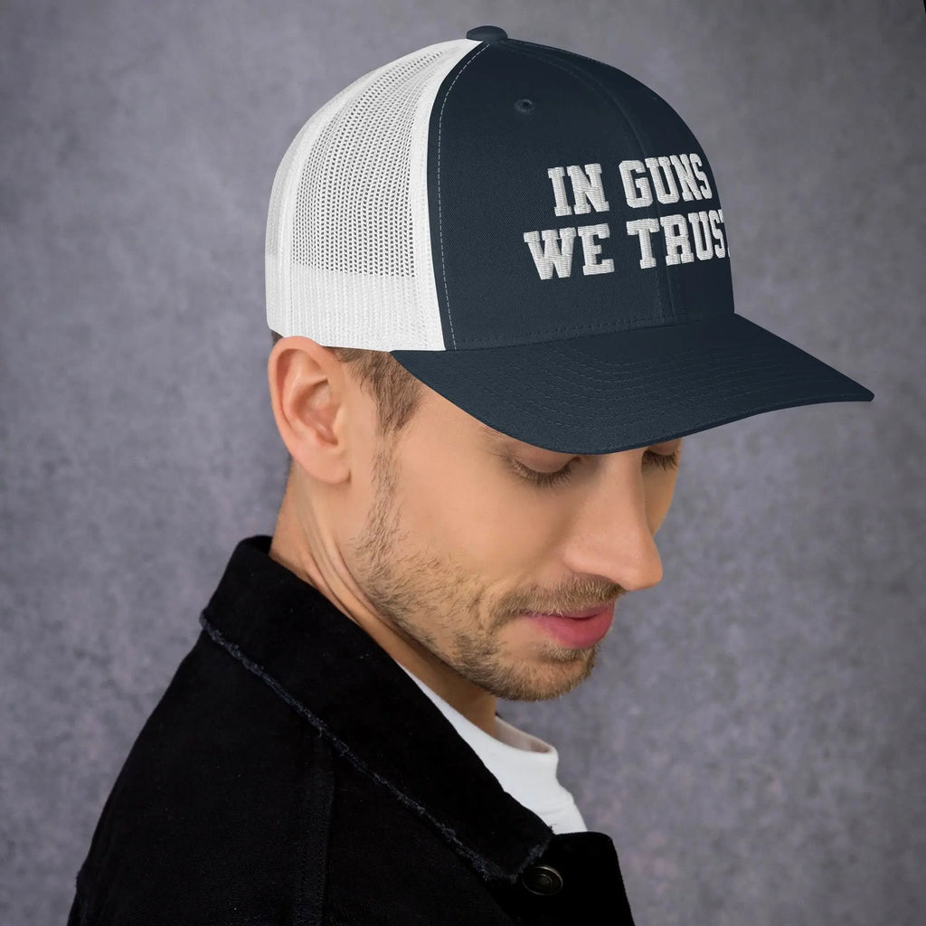 Man wearing a cap with 'IN GUNS WE TRUST' text on a gray background