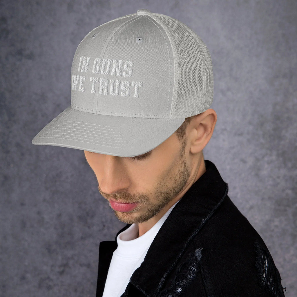 Person wearing a gray cap with 'IN GUNS WE TRUST' text on a dark background