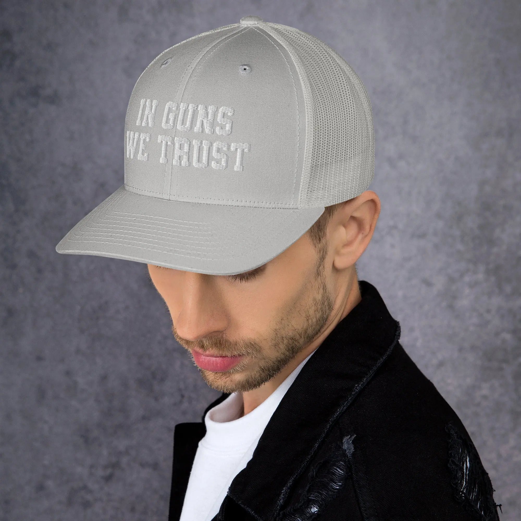 Person wearing a gray cap with 'IN GUNS WE TRUST' text on a dark background