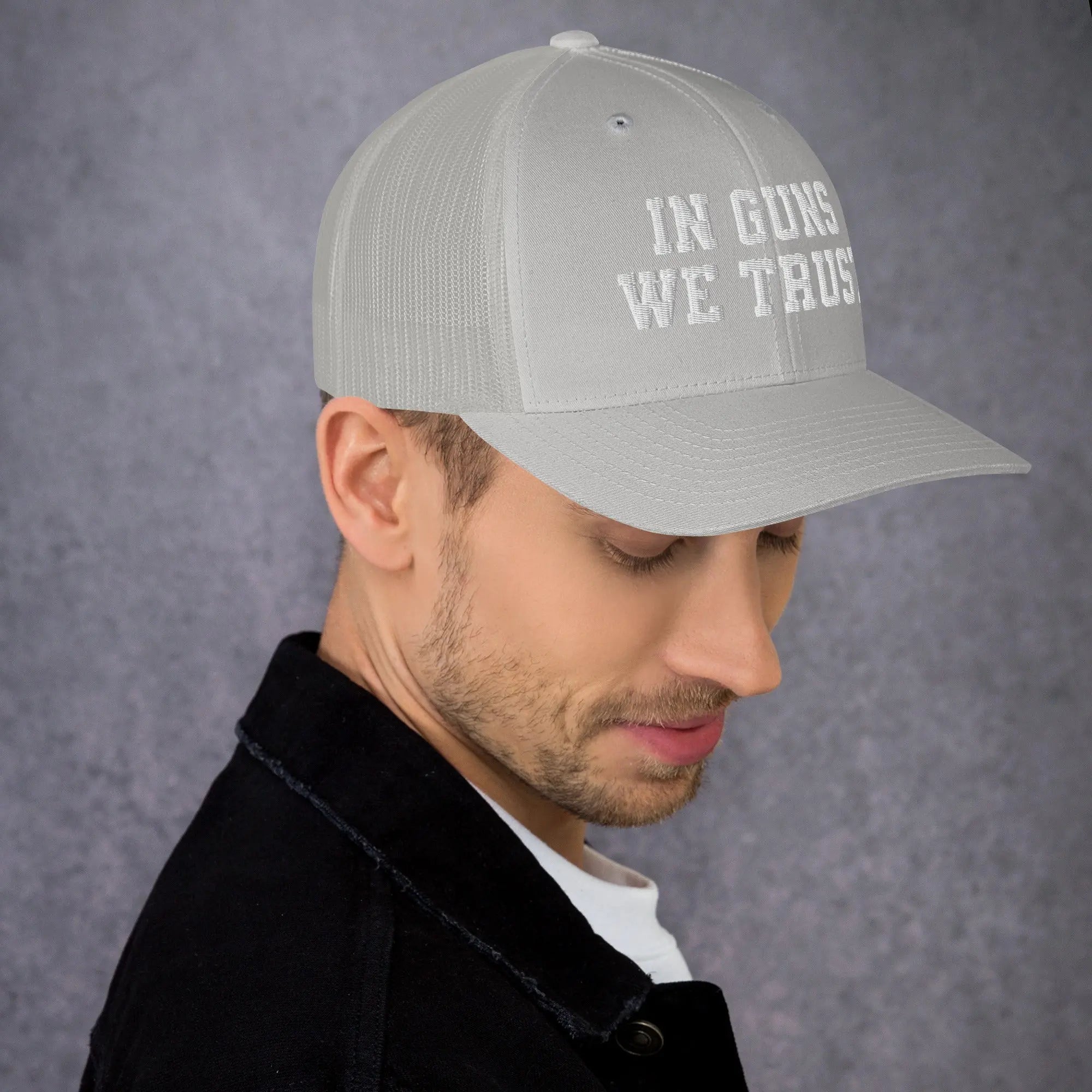 Man wearing a gray cap with 'IN GUNS WE TRUST' text on a gray background