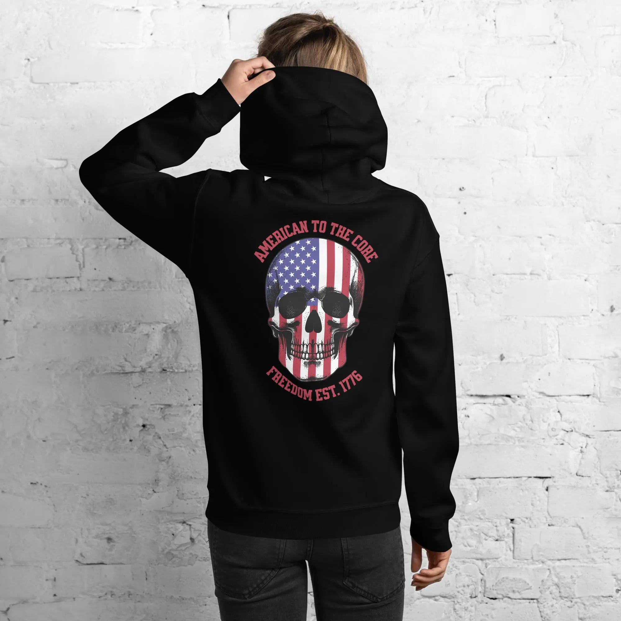 Back of a woman wearing a black patriotic hoodie with a skull and the text "American to the core. Freedom Est. 1776." 