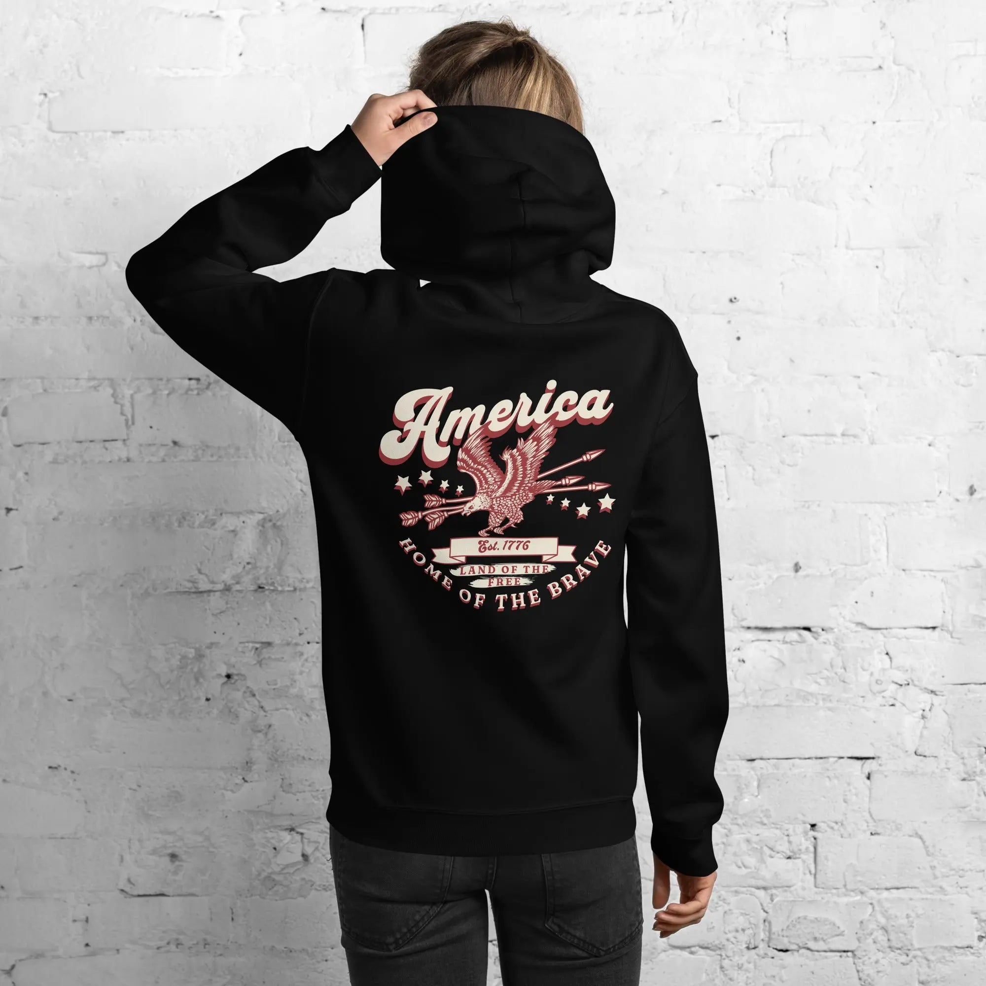 Back of a woman wearing a black patriotic hoodie with an eagle and the text "America home of the brave." 