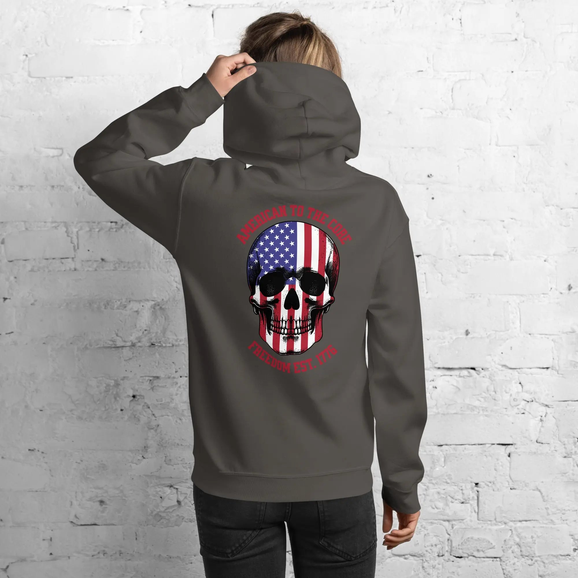 Back of a woman wearing a charcoal patriotic hoodie with a skull and the text "American to the core. Freedom Est. 1776." 