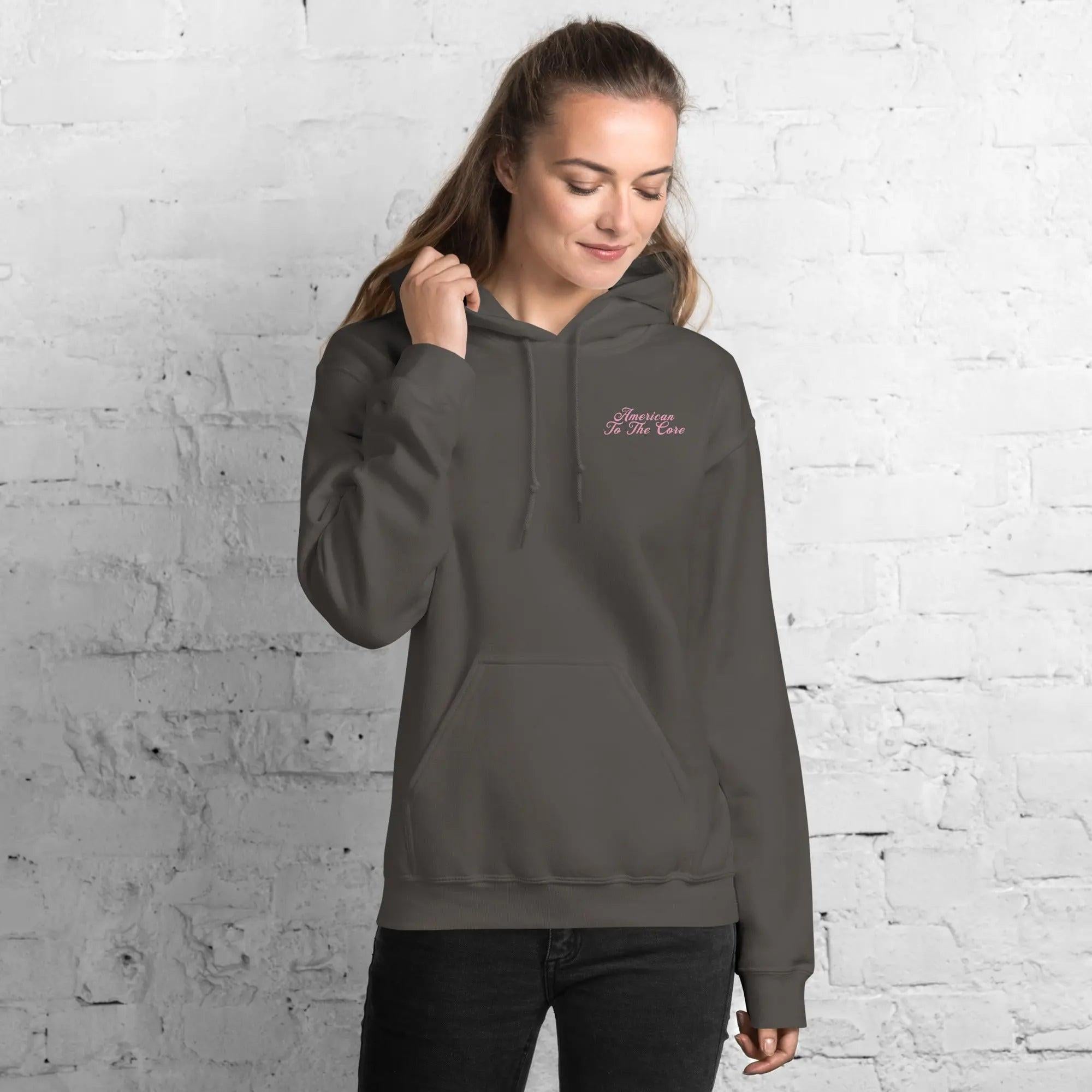A woman wearing a charcoal patriotic hoodie with the text "American To The Core"