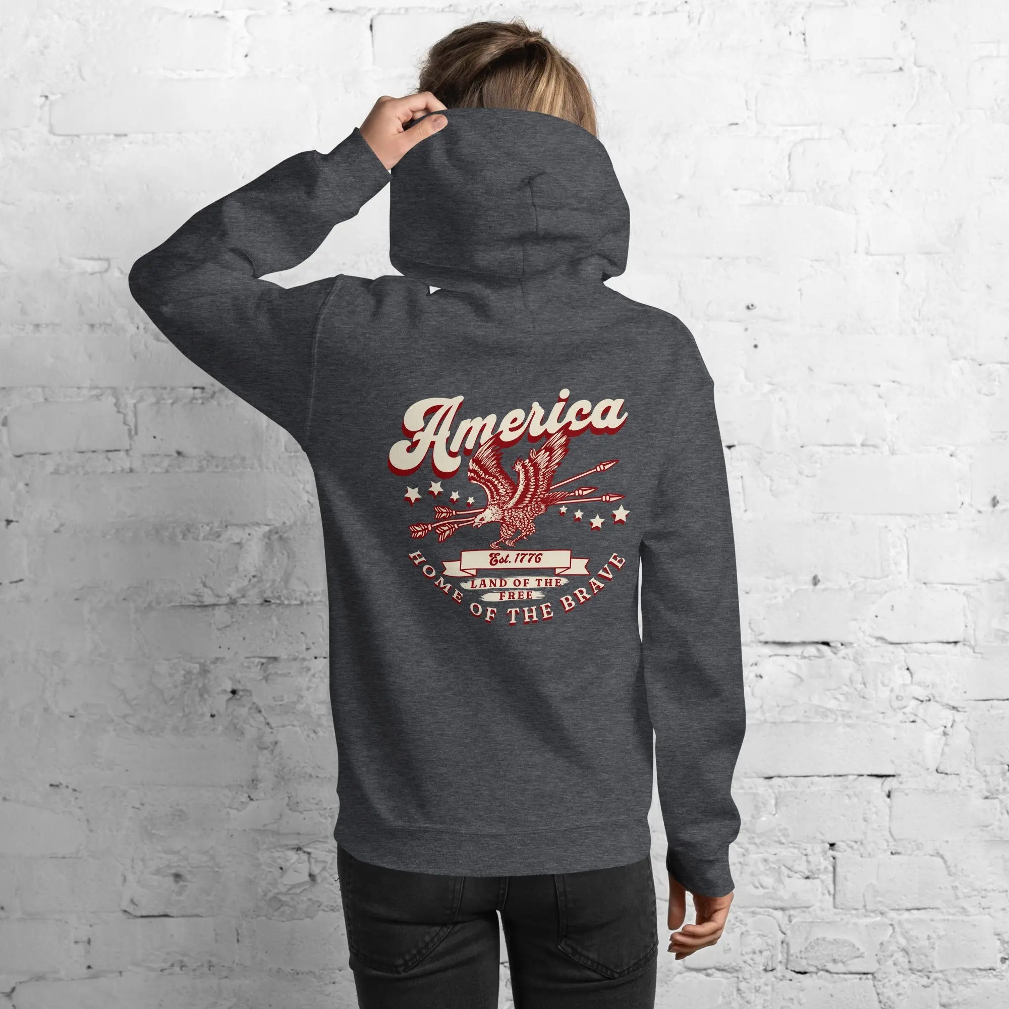 Back of a woman wearing a dark heather patriotic hoodie with an eagle and the text "America home of the brave."