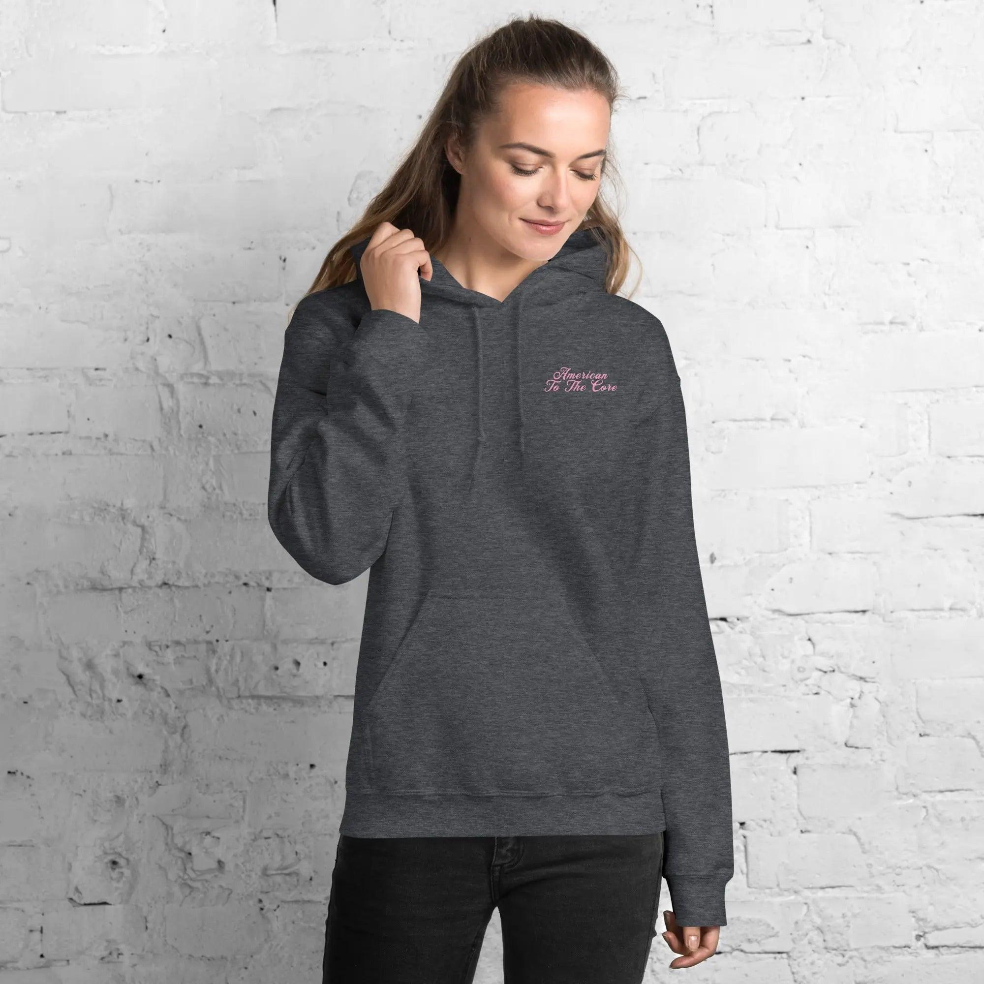 A woman wearing a dark heather patriotic hoodie with the text "American To The Core"