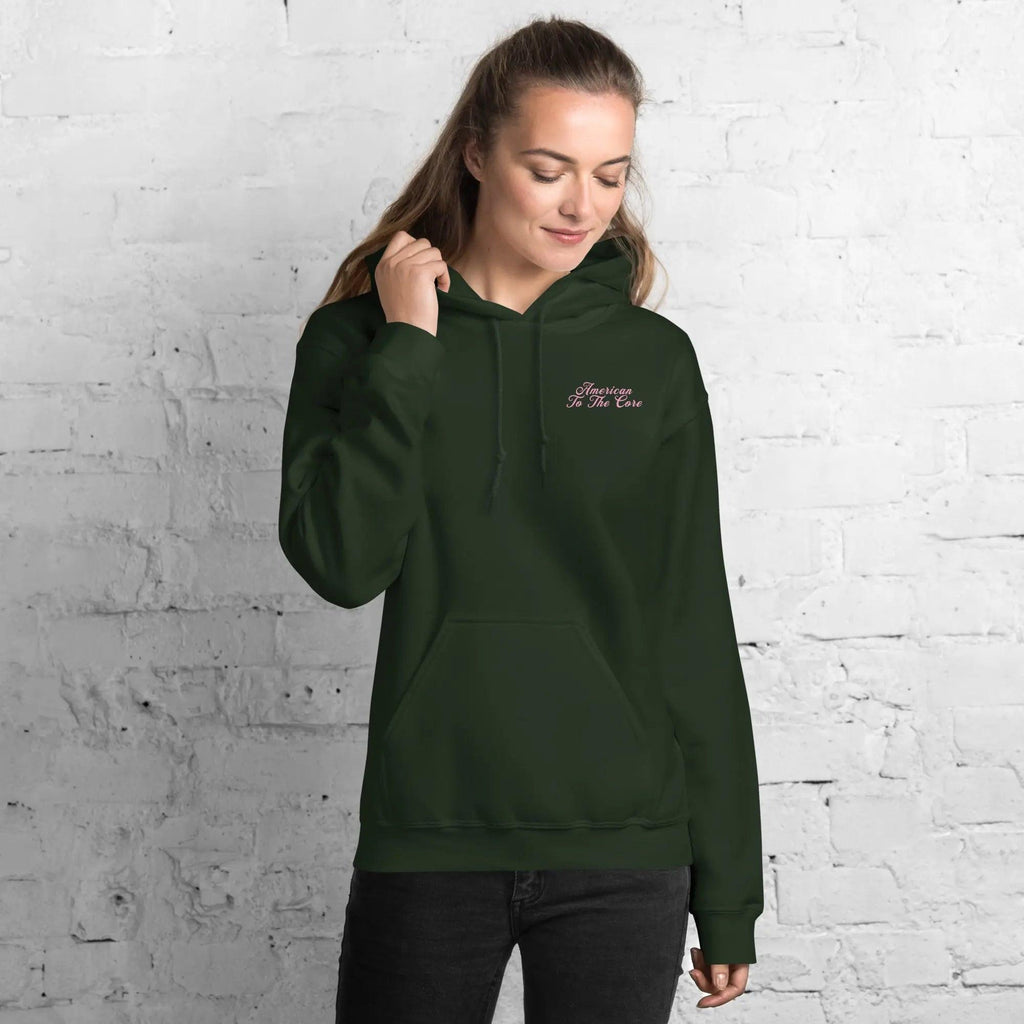 A woman wearing a forest green patriotic hoodie with the text "American To The Core"
