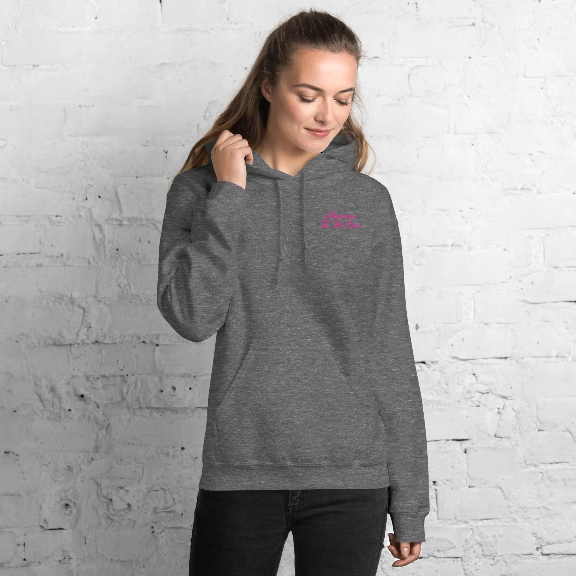 A woman wearing a patriotic graphite heather hoodie with the text "American To The Core" in pink.
