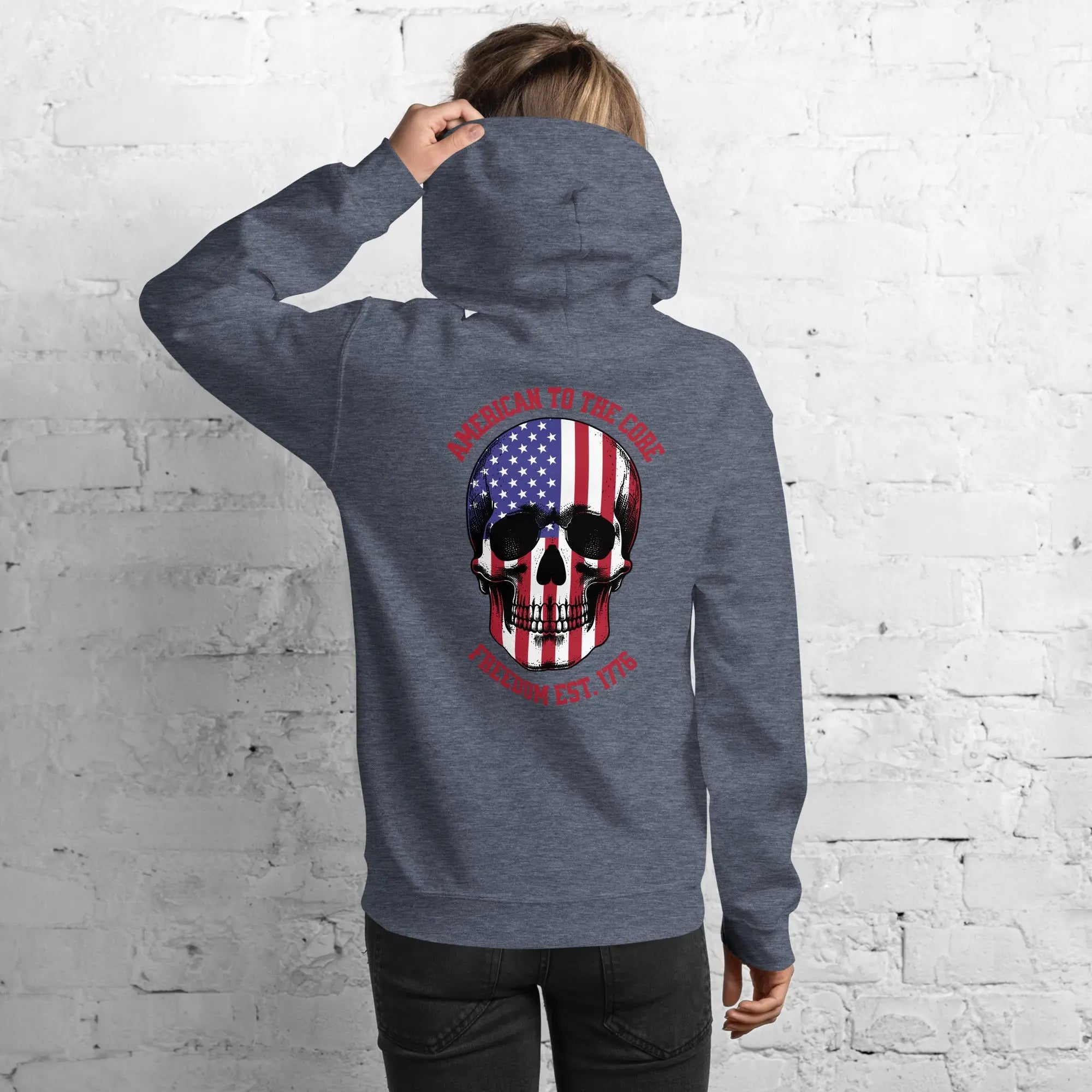 Back of a woman wearing a heather sport patriotic hoodie with a skull and the text "American to the core. Freedom Est. 1776." 
