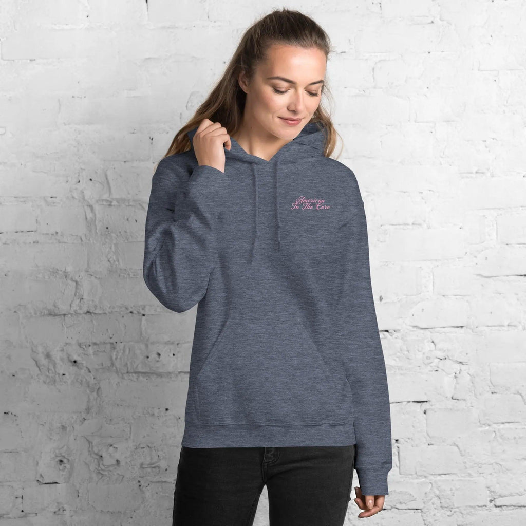 A woman wearing a heather-sport patriotic hoodie with the text "American To The Core"