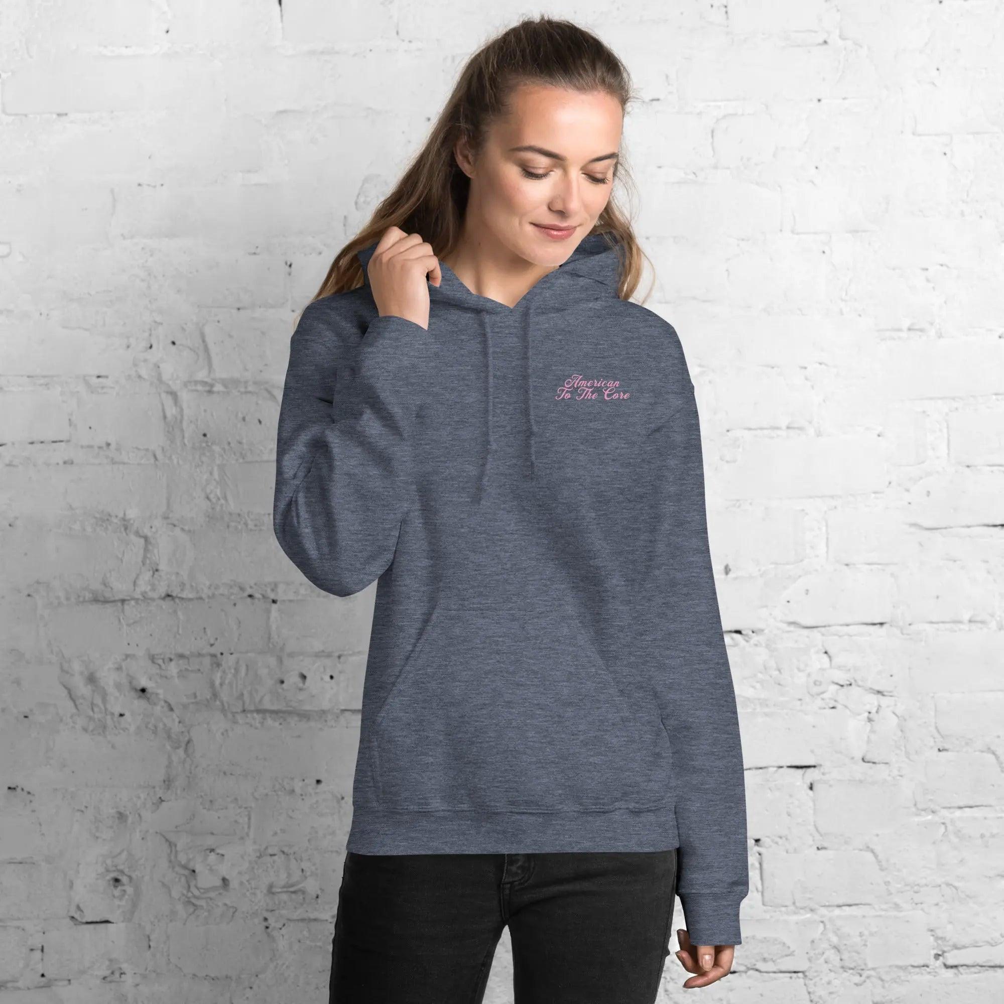 A woman wearing a heather-sport patriotic hoodie with the text "American To The Core"