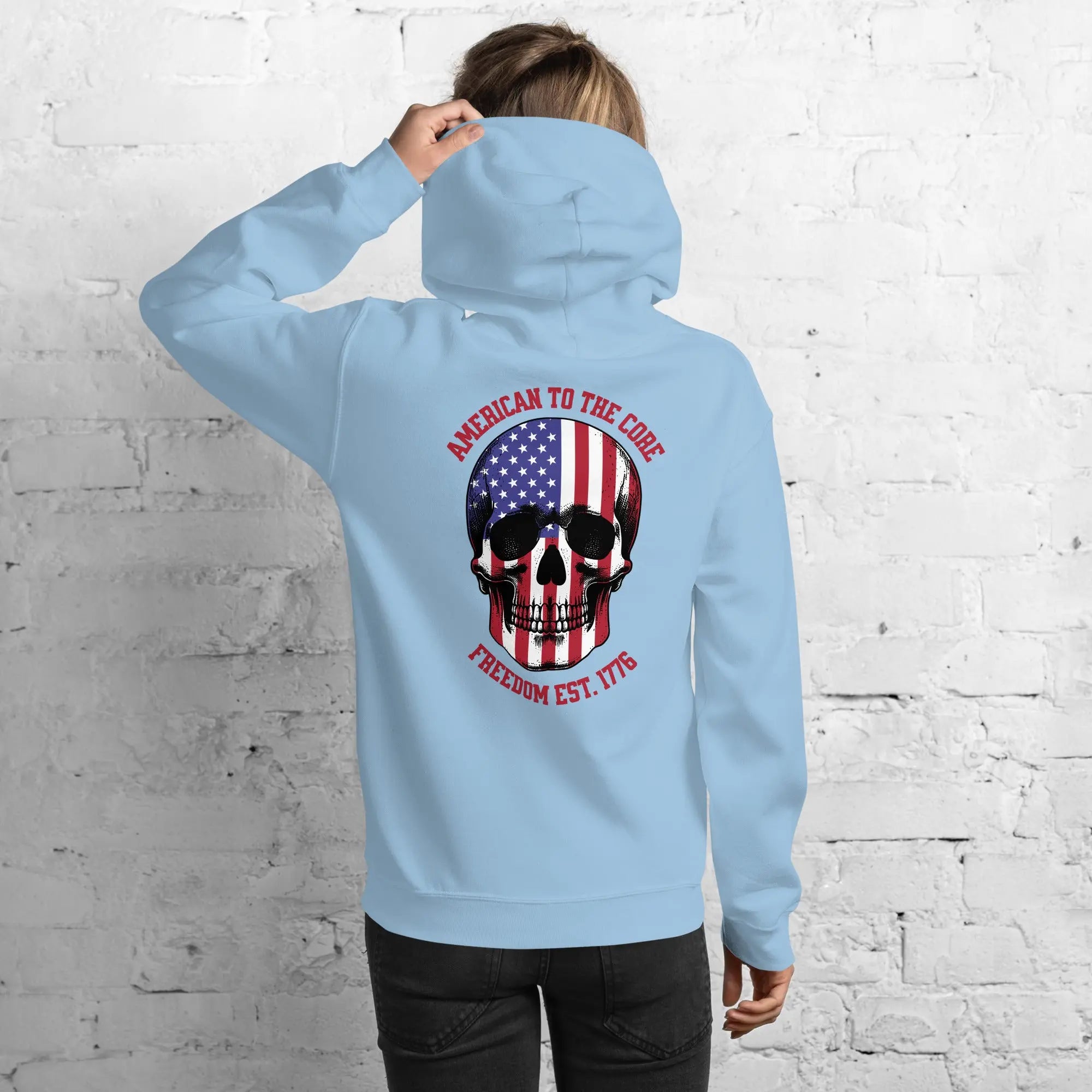 Back of a woman wearing a light blue patriotic hoodie with a skull and the text "American to the core. Freedom est. 1776." 