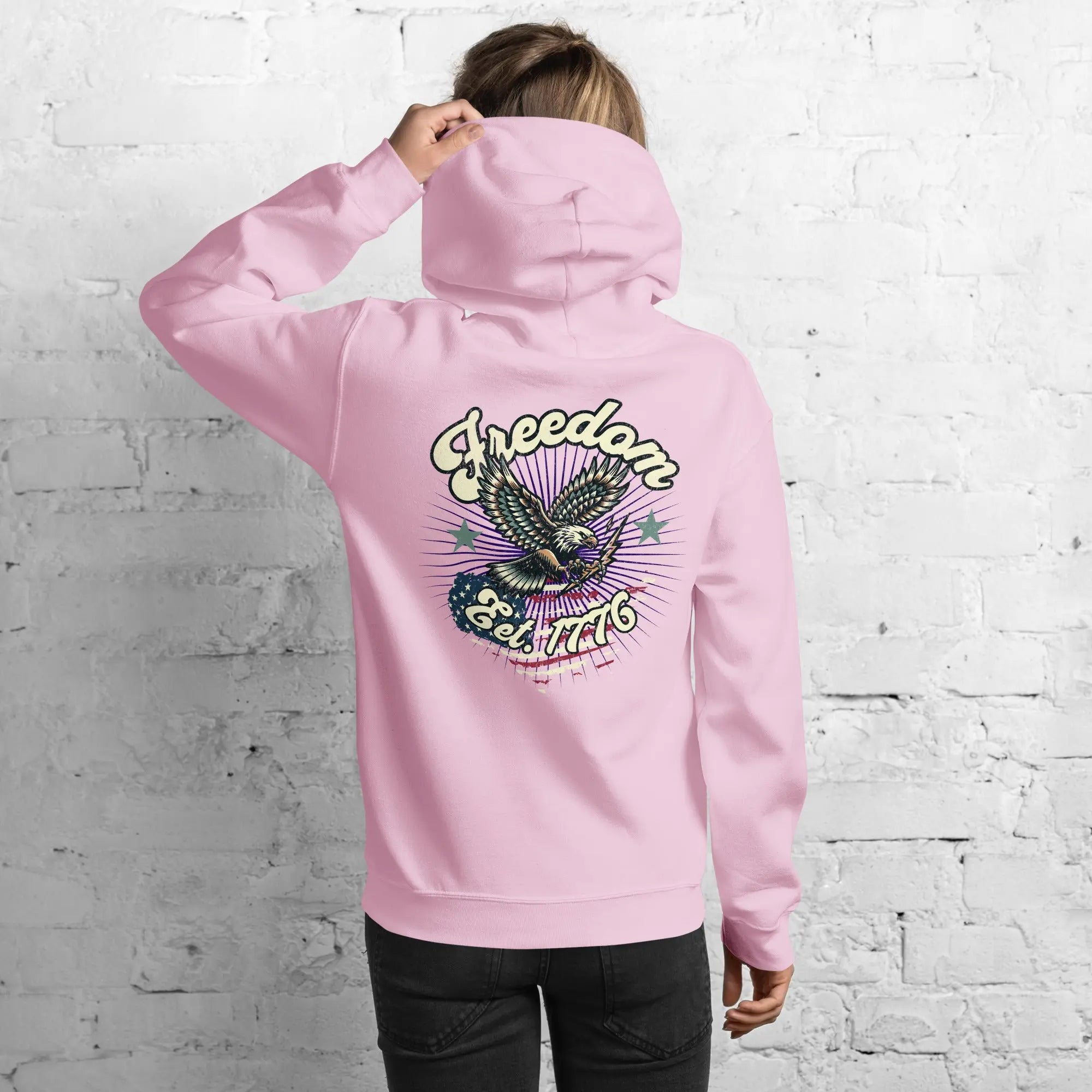 Back of woman wearing a light pink patriotic hoodie with an eagle and the text "Freedom Est. 1776" 