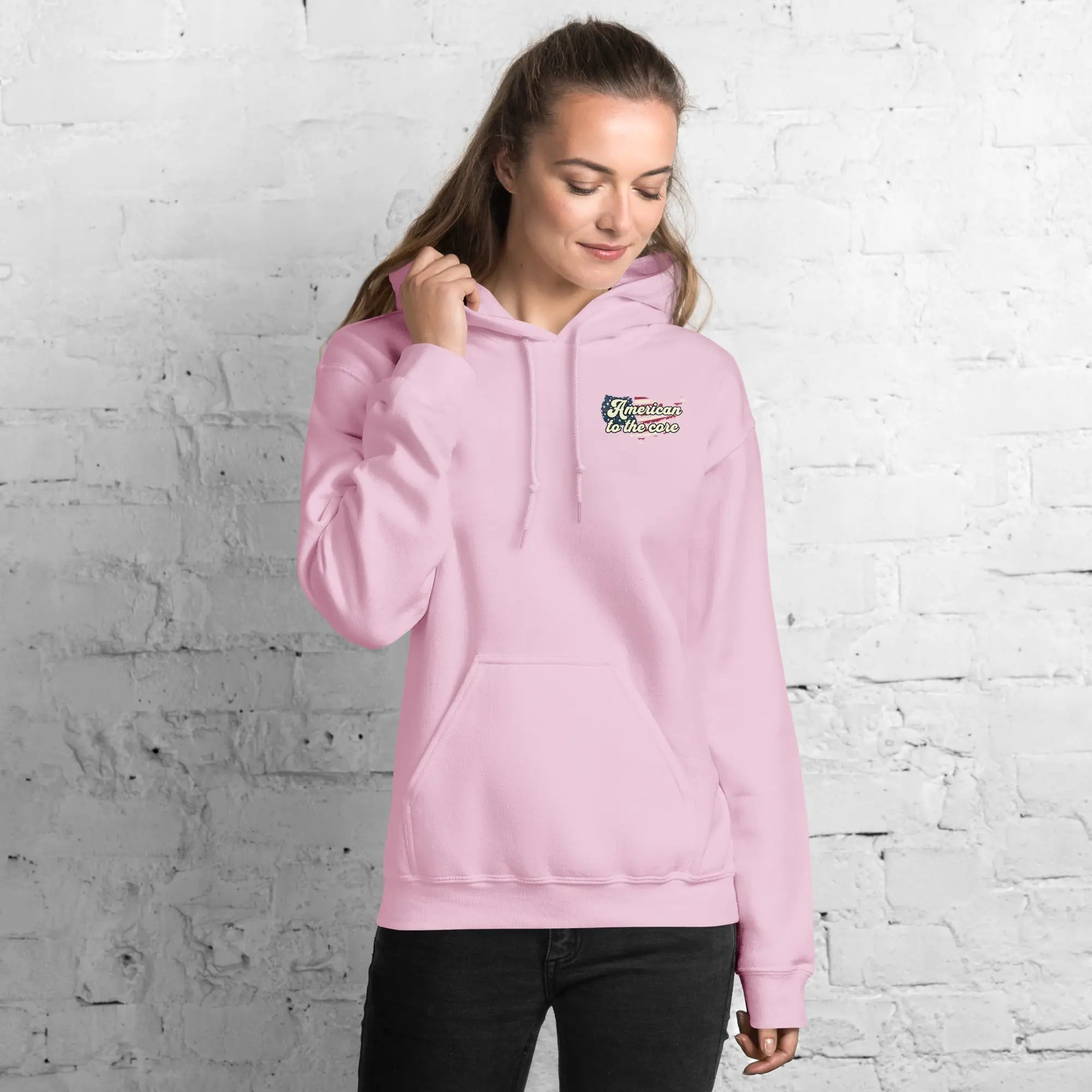 Woman wearing a light pink patriotic hoodie with the text "American to the core" 